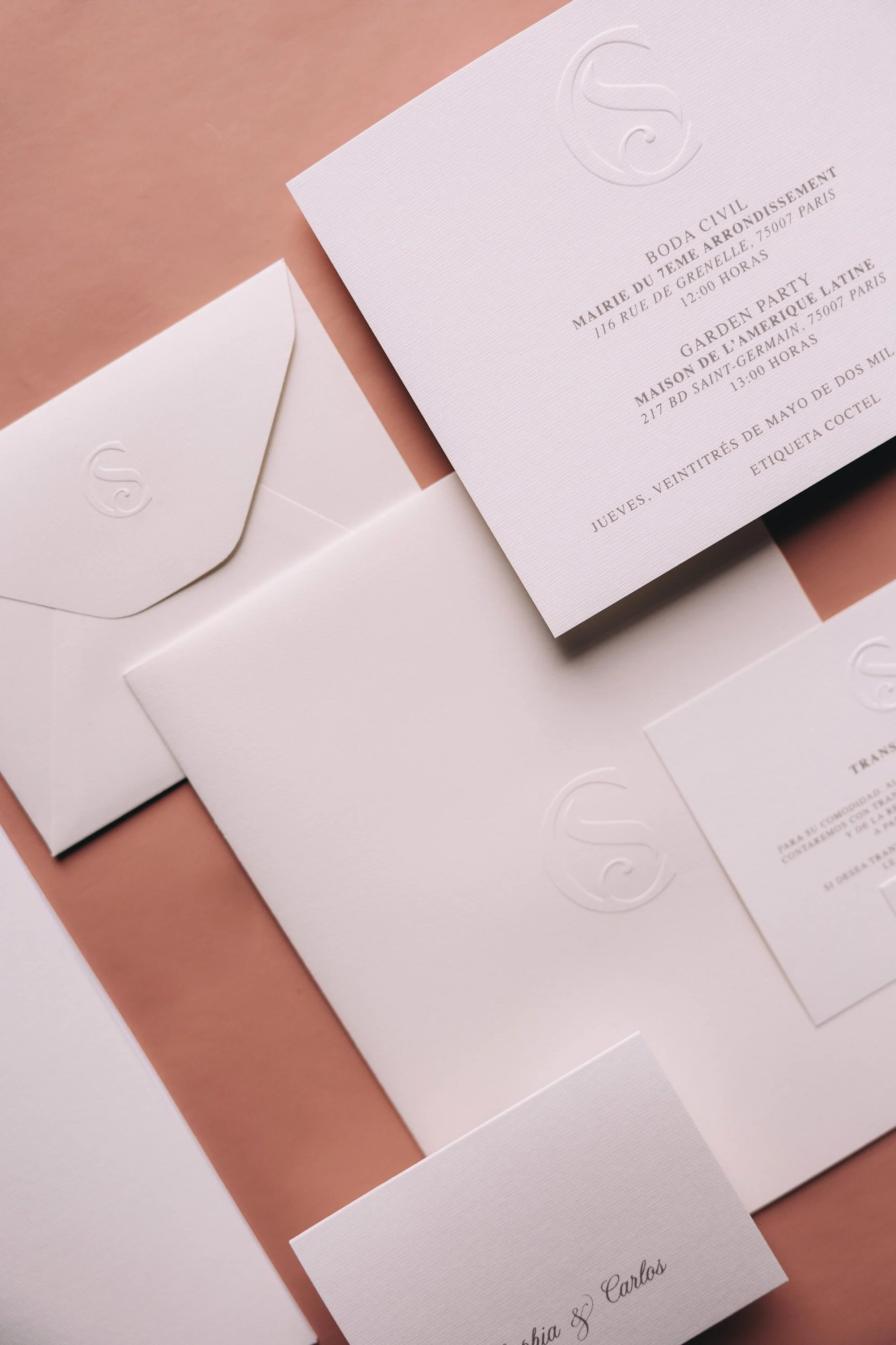Wedding invitation set with embossed logo, an envelope, and a card with the names 'Sofia & Carlos' on clear textured paper.