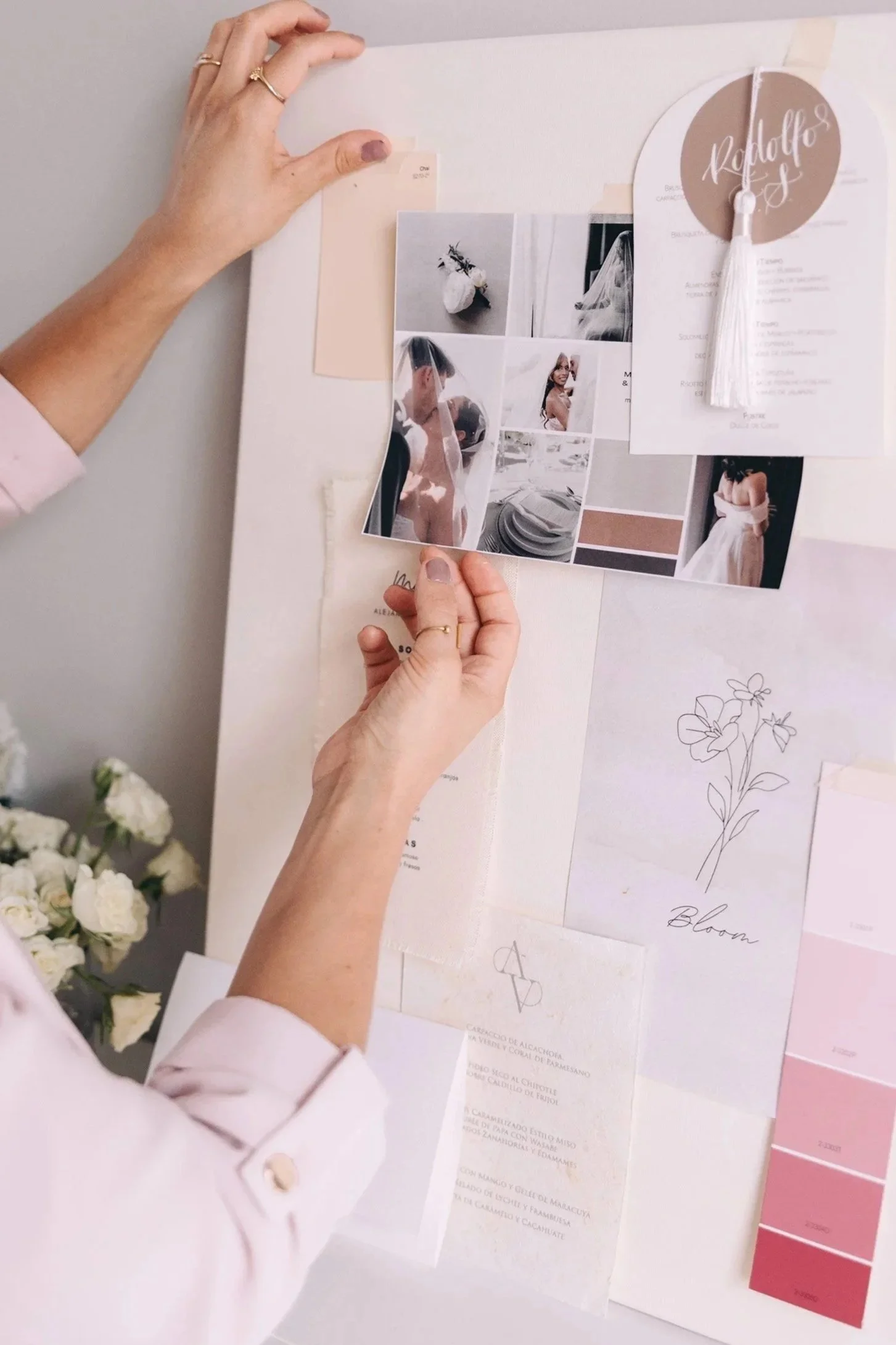 A person arranging a mood board with photos, color swatches, and sketches on a wall, possibly planning a wedding or event.