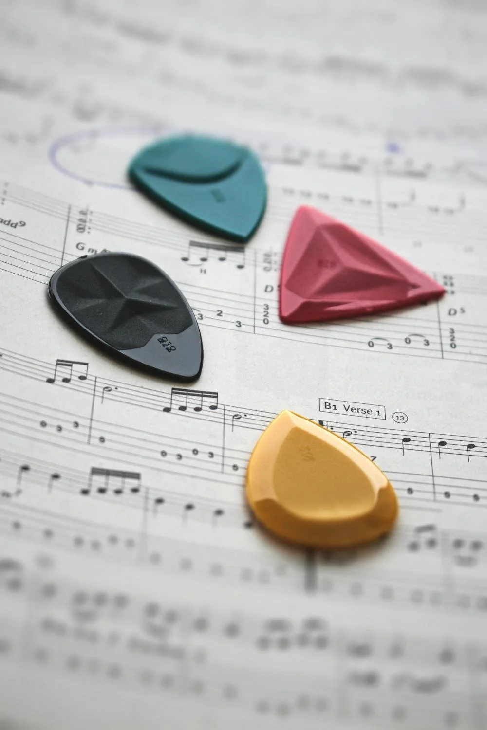 Cinque plettri colorati (blu, rosa, nero, giallo) posati su una partitura musicale.
