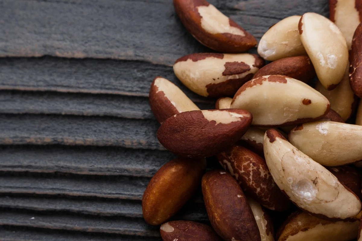 A close-up of mixed pine nuts on a dark textured surface.