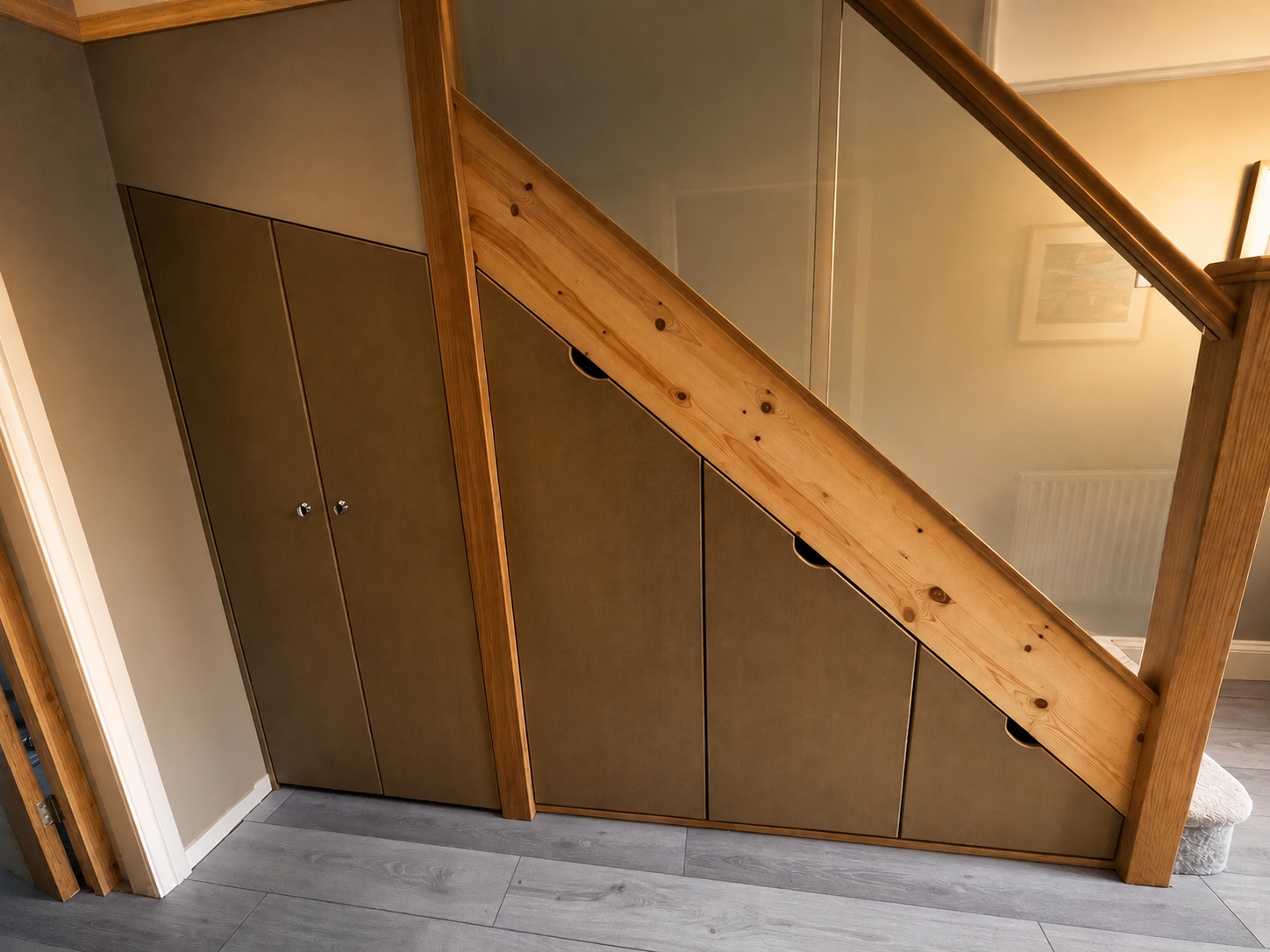 Under-stair storage with brown cabinet doors and a wooden railing on top, in a room with light-colored walls and wood flooring.
