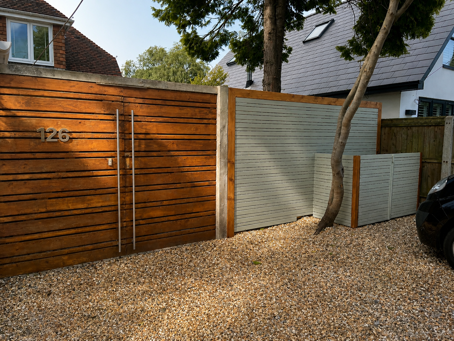 Modern house exterior with a wooden gate, house number 126, a tree growing nearby, and gravel ground