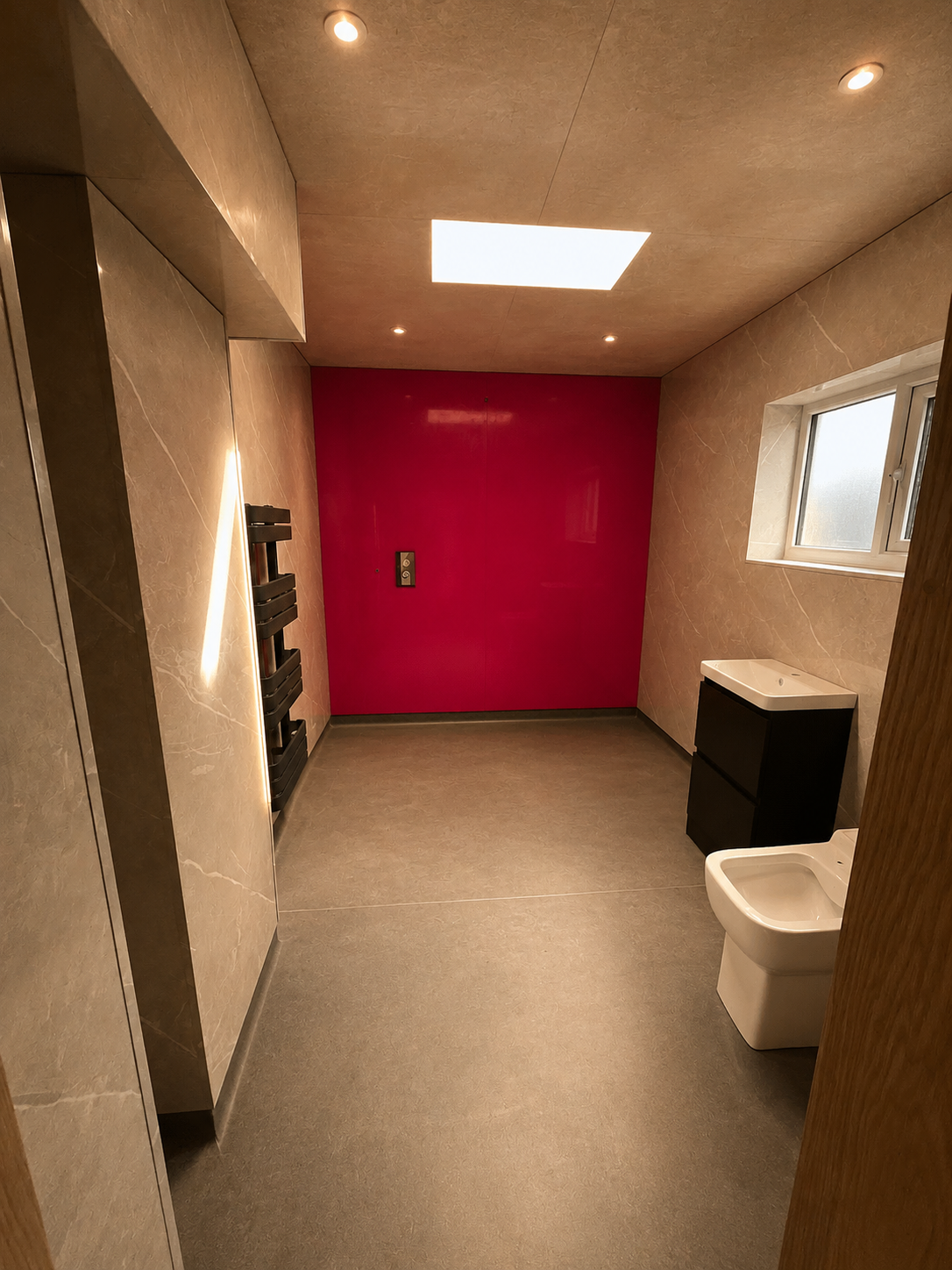 Empty bathroom with gray floor and walls, a window, a small black sink with cabinet, a wall-mounted bidet, a pink accent wall, a small window, and recessed lighting.