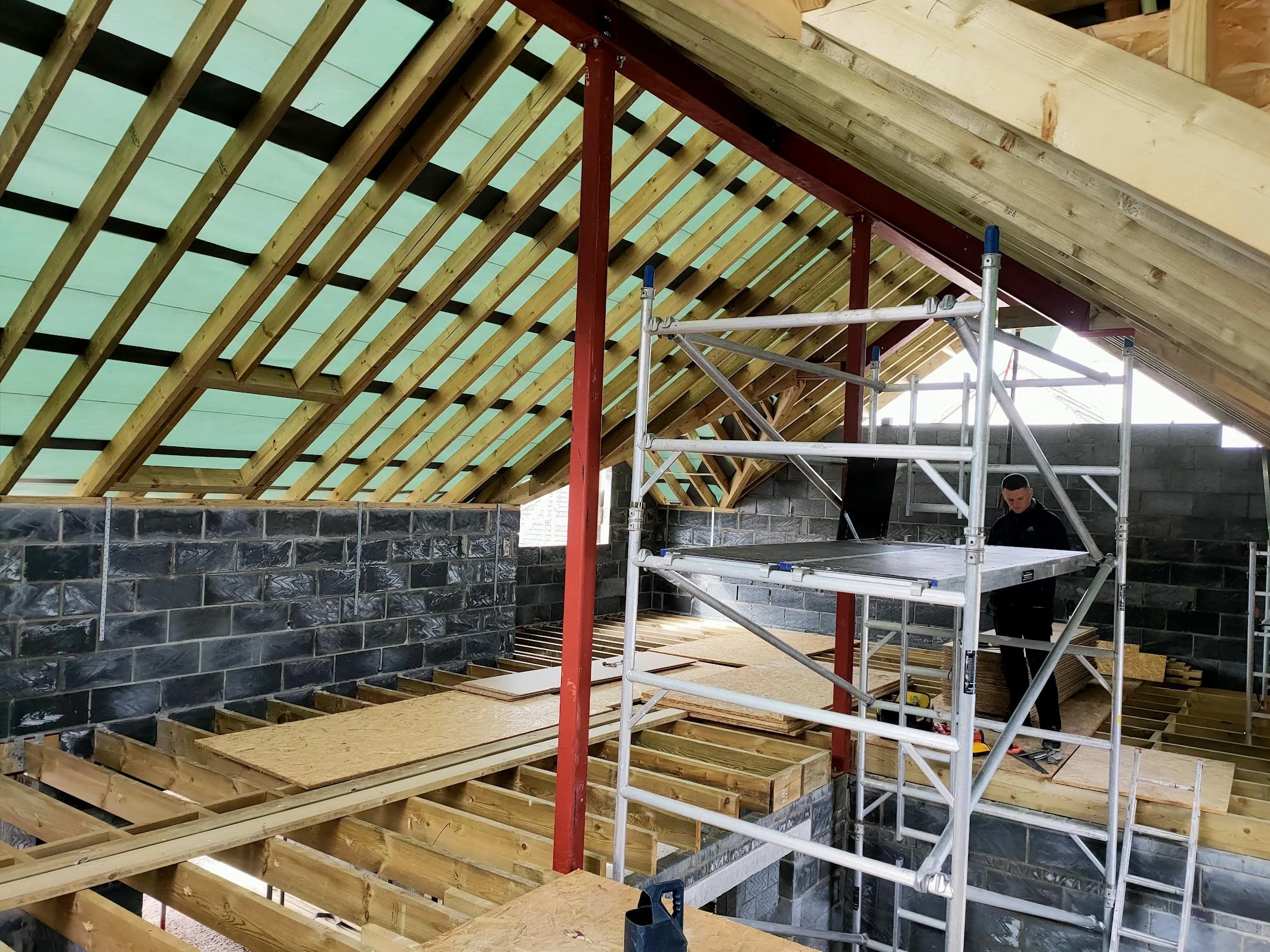 Construction site with wooden roof framing, scaffolding, and a worker.