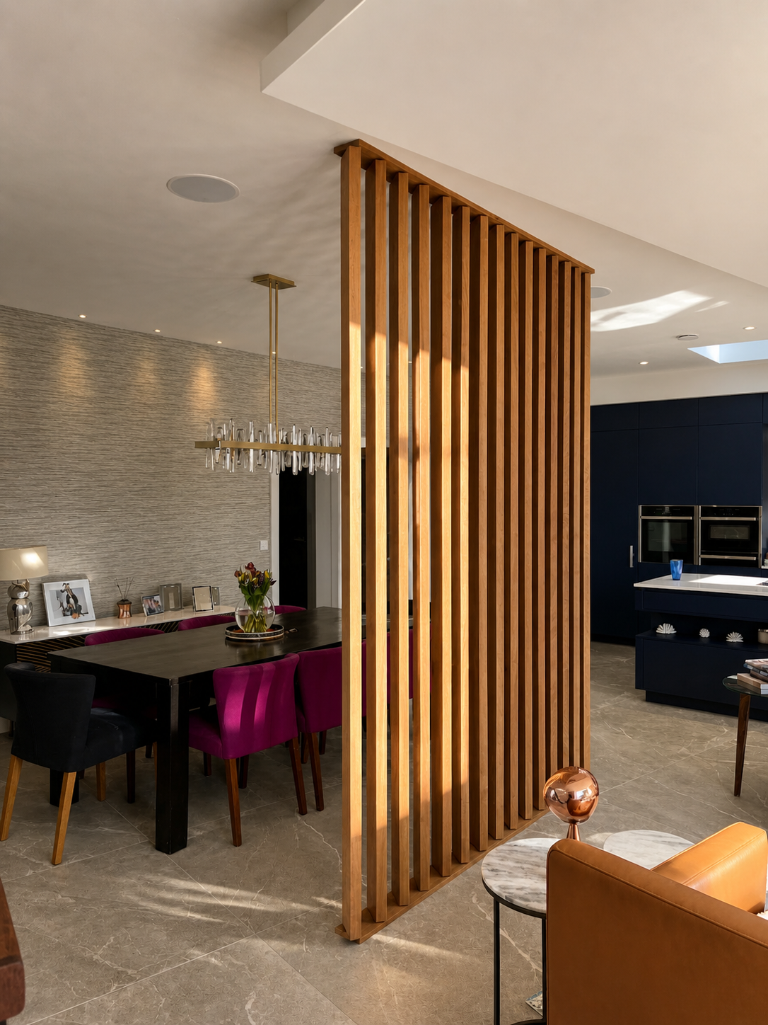 Modern dining and living area separated by a wooden slat room divider, with a black dining table, purple and black chairs, and a chandelier, in a contemporary home.