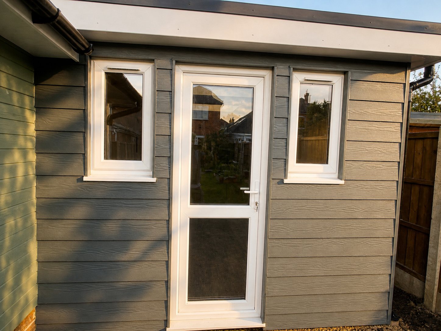 Backyard view through a white framed glass door with two small side windows, surrounded by wooden siding, some of which is painted green.