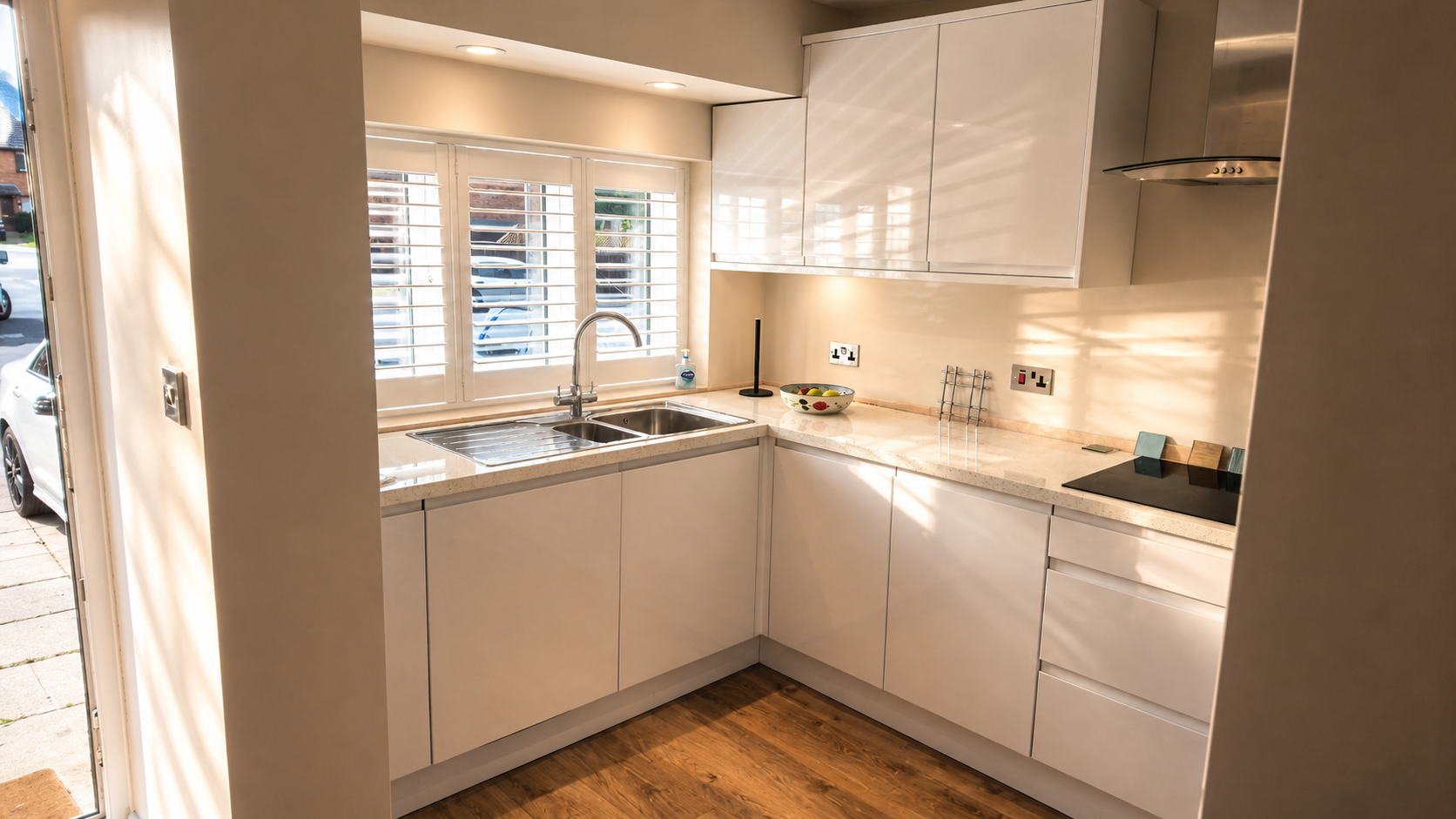 Modern kitchen with white cabinets, marble countertop, stainless steel sink, and window with shutters