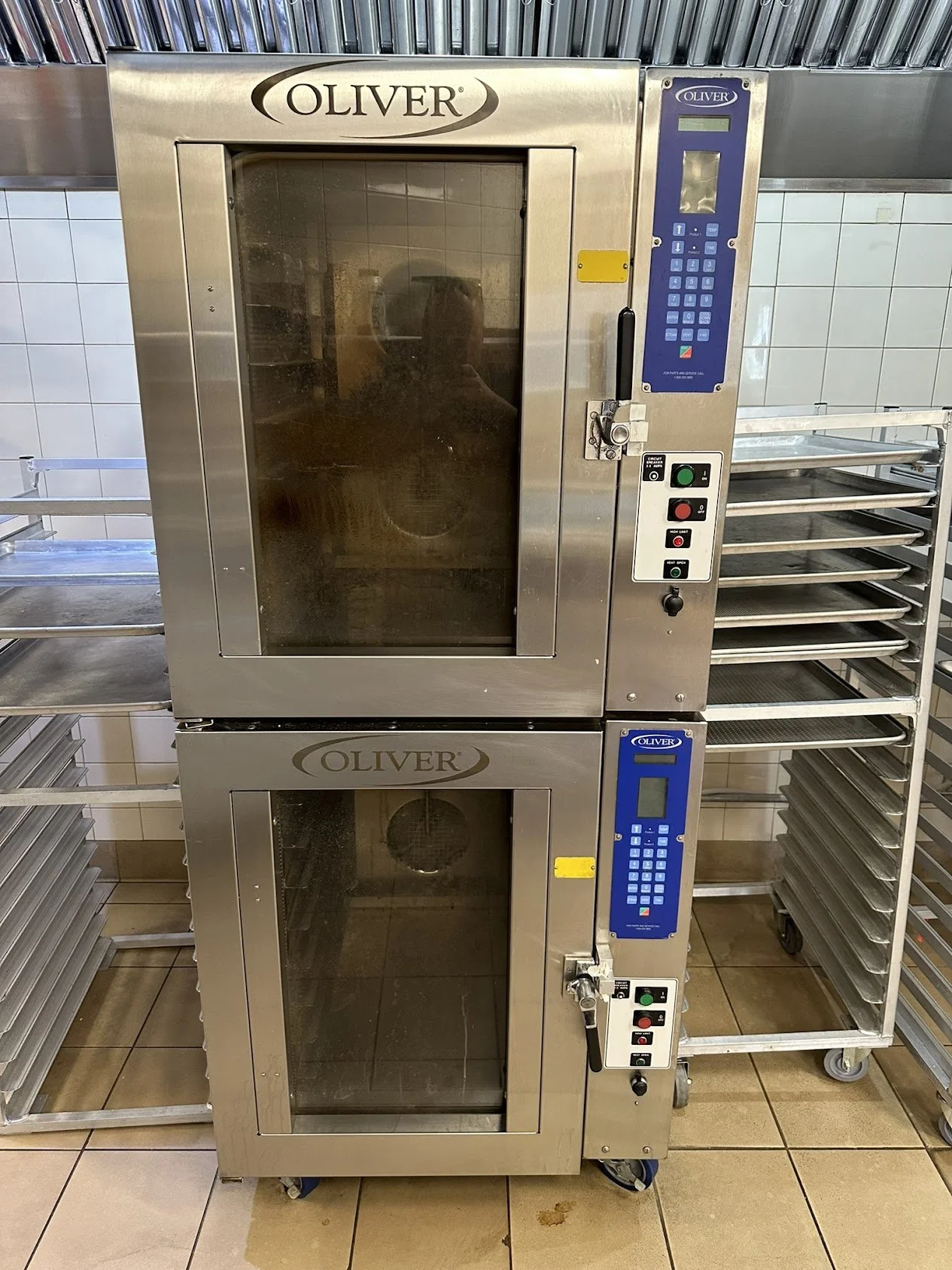 Two stainless steel commercial convection ovens stacked vertically in a restaurant kitchen, with control panels and wheels for mobility, branded as Oliver.