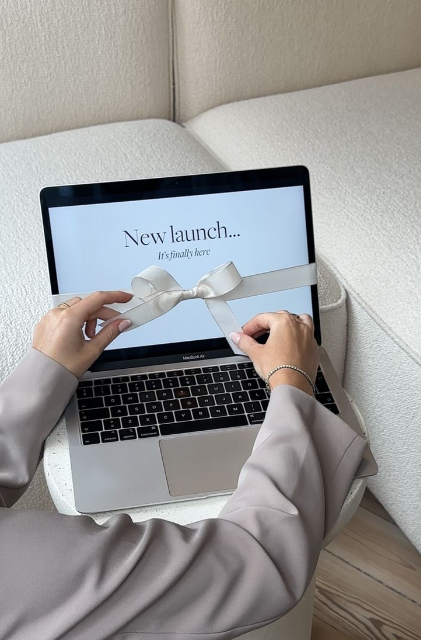 A person is opening a laptop displaying a message that reads 'New launch... It's finally here' with a ribbon and bow on the screen indicating a new product release.