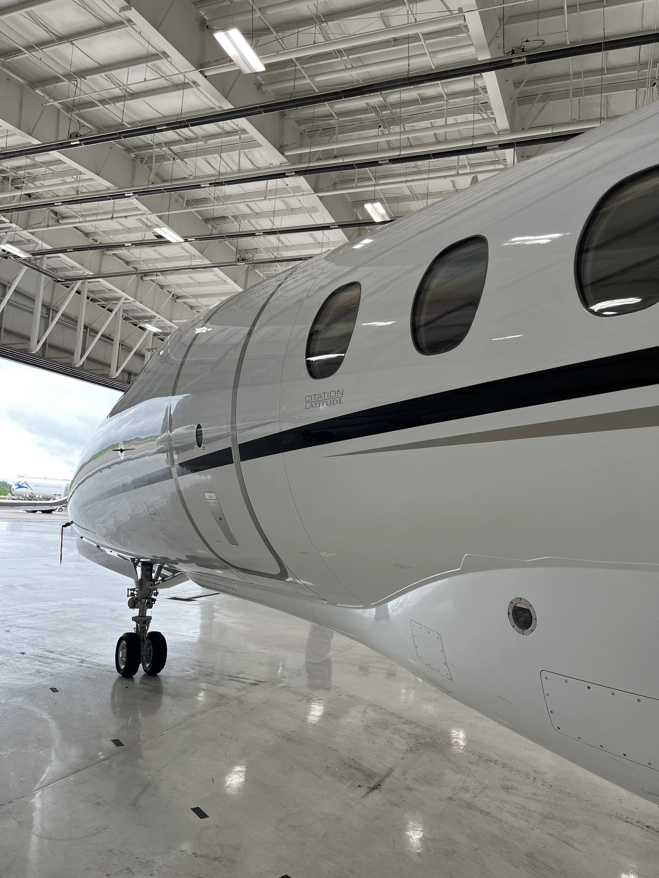 A private jet inside an aircraft hangar with a smooth white exterior, visible windows, and landing gear.