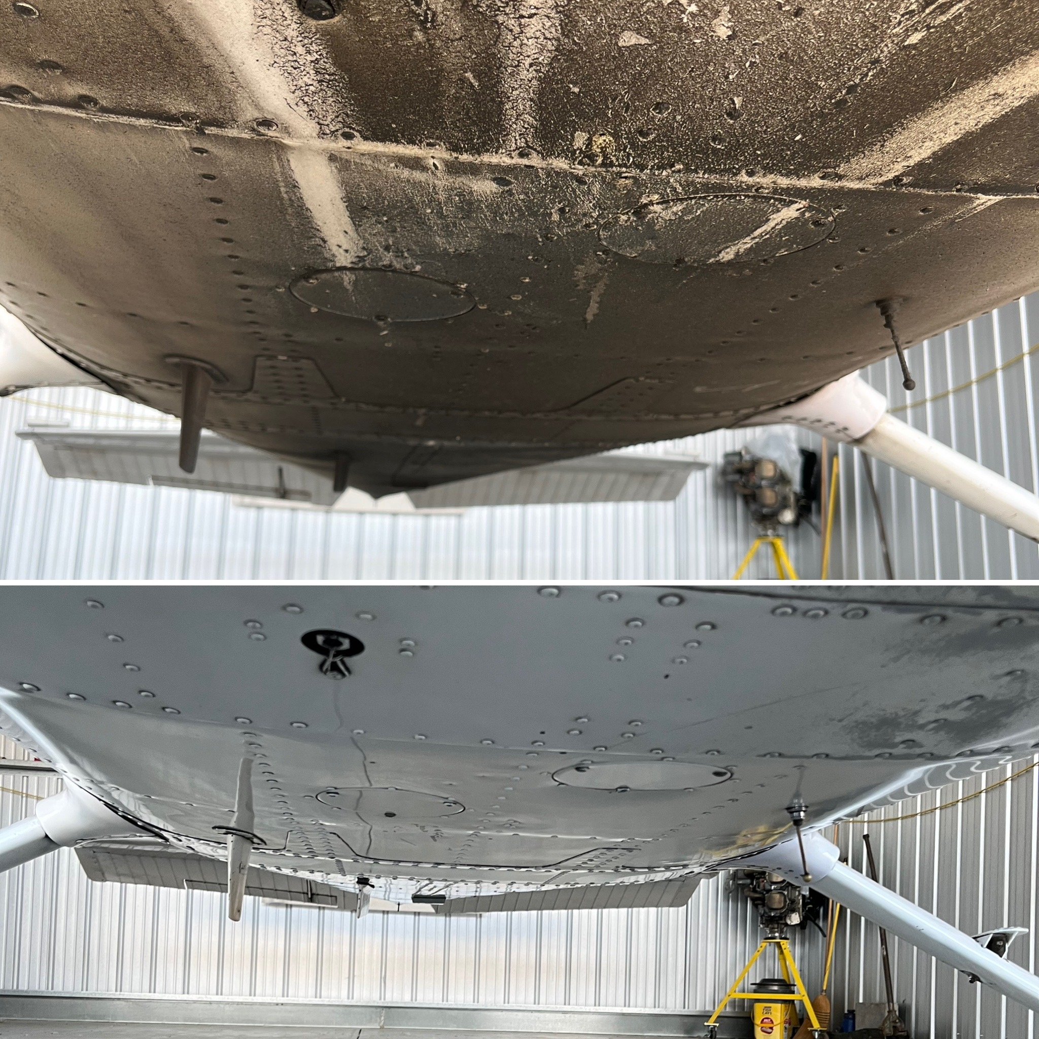 The underside of an airplane wing, showing rivets, panels, and two circular access hatches, with a yellow ladder and other equipment in a hangar.