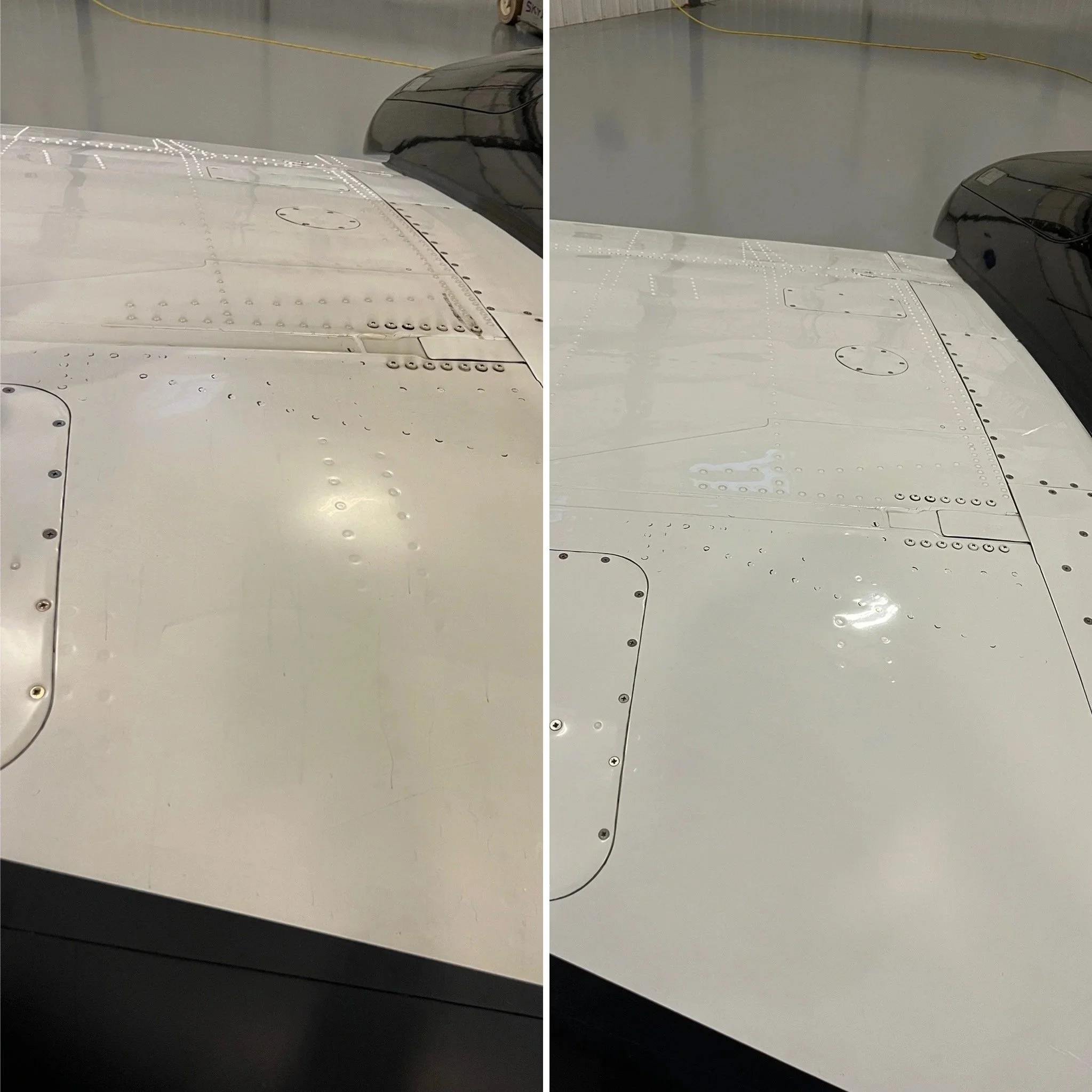 Close-up of an aircraft's wing showing detailed rivets and panels, with a smooth surface and a black sensor or antenna at the wingtip, inside a hangar with a concrete floor and yellow cable in the background.