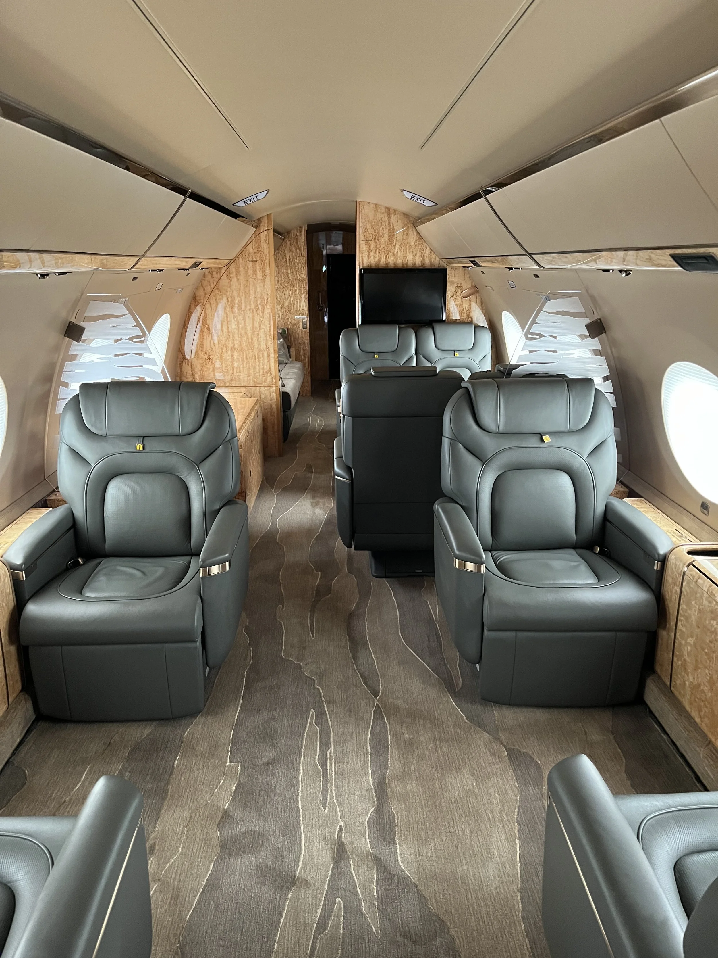 Interior of a private jet with leather seats, a large flat screen TV, and wood paneling on the walls.