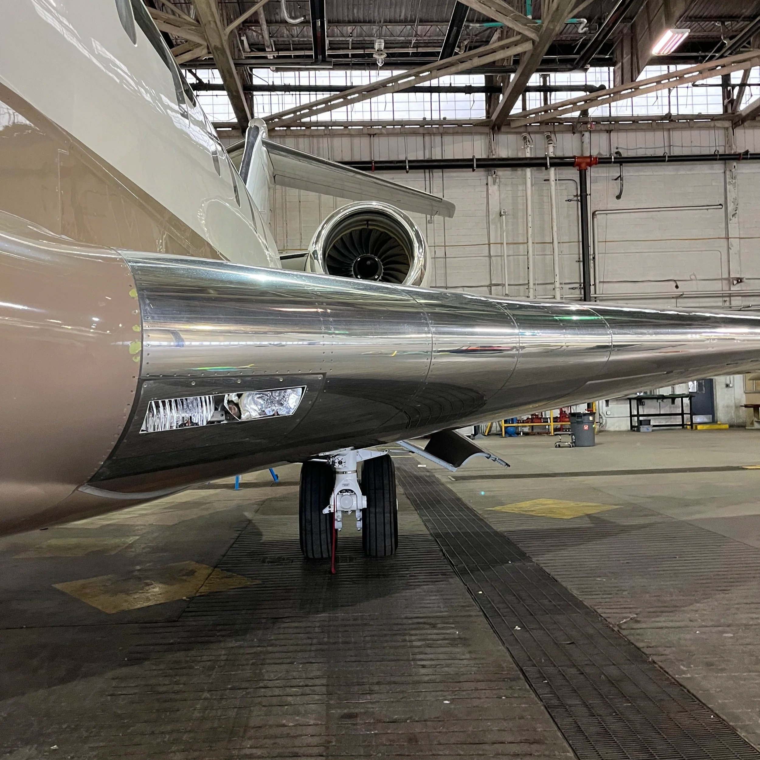 View of an airplane in a hangar with a jet engine, stairs, and industrial equipment visible.