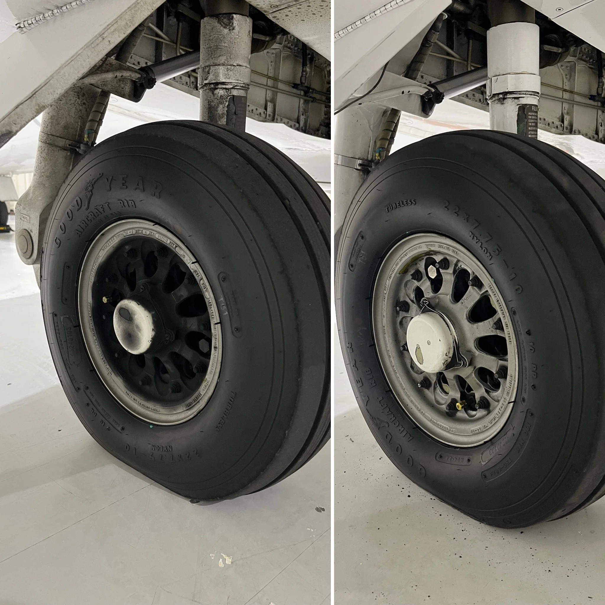 Close-up of an airplane landing gear wheel, showing signs of wear and dirt, with a manufacture label. The background shows a smooth white floor with minor debris.