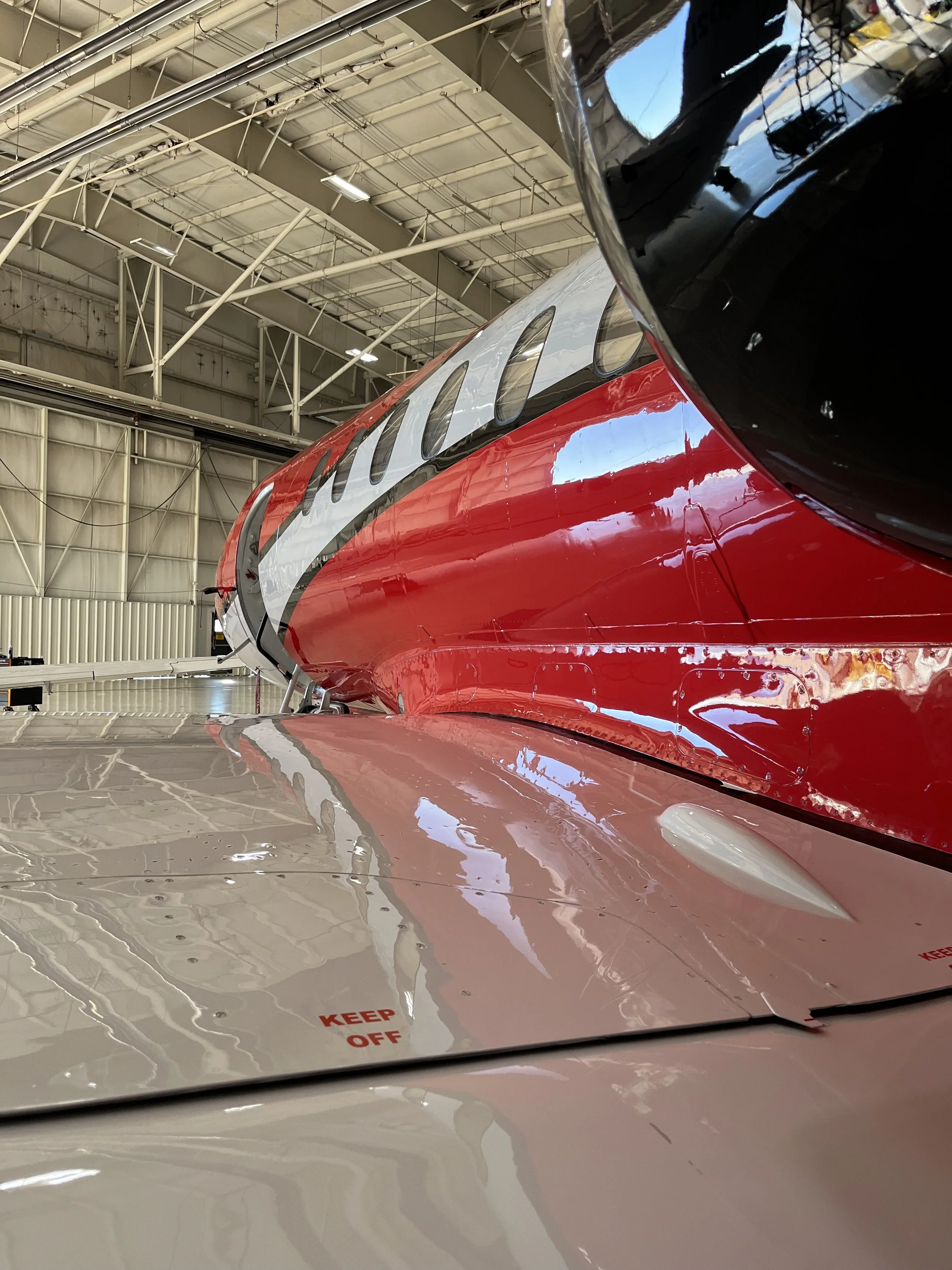 Close-up of a colorful train inside a hangar with a reflective surface and some warning text in red that says, 'KEEP OFF'.