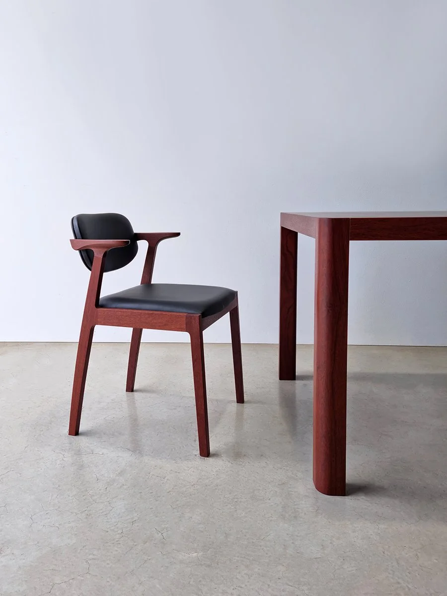 Kinross Chair in rich red-toned Jarrah with black leather upholstery beside a matching Jarrah table - bespoke furniture by Nathan Day Design