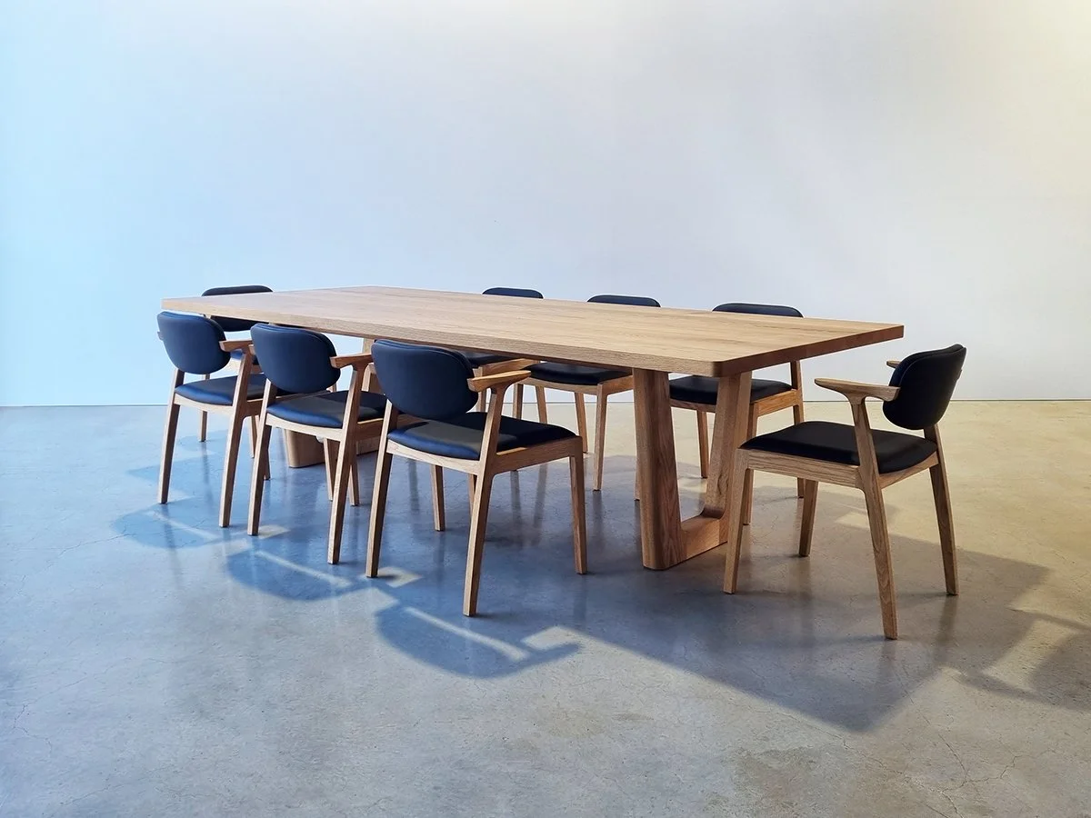 Clairault Table in American Oak set with eight navy upholstered timber-armed dining chairs, bright studio setting - bespoke furniture by Nathan Day Design