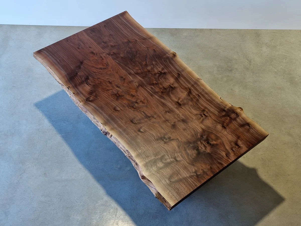 Overhead view of a live edge slab showing dramatic burled figure and dark rich grain, casting shadow on concrete floor - Nathan Day Design