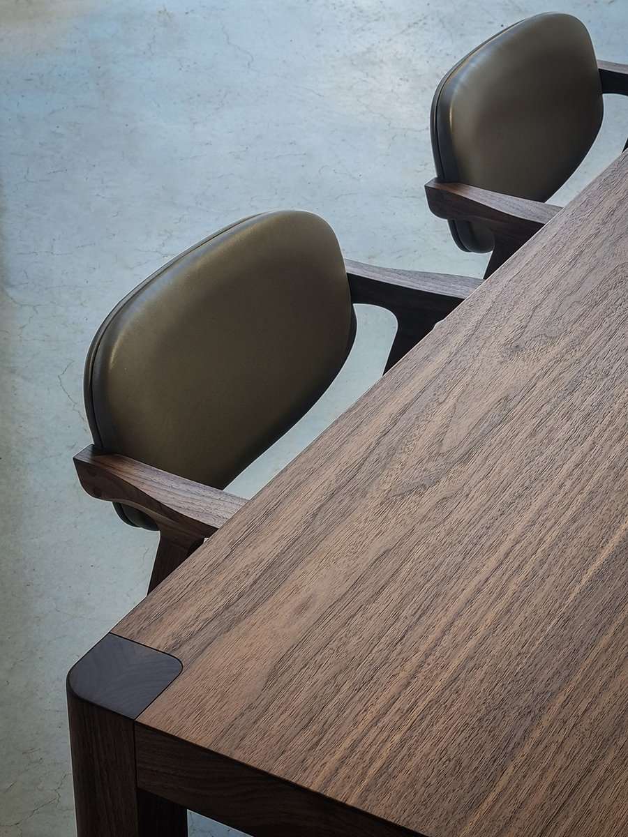 Close-up angled detail of Irvine Table corner in dark Walnut with olive-green leather dining chairs - bespoke furniture by Nathan Day Design