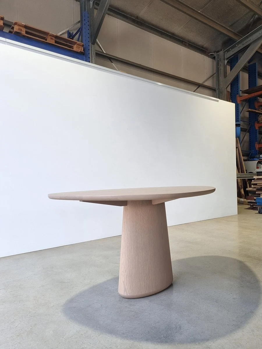 Angled three-quarter view of Pebble Table in grey-tinted American Oak showing organic tabletop silhouette, workshop setting - bespoke furniture by Nathan Day Design