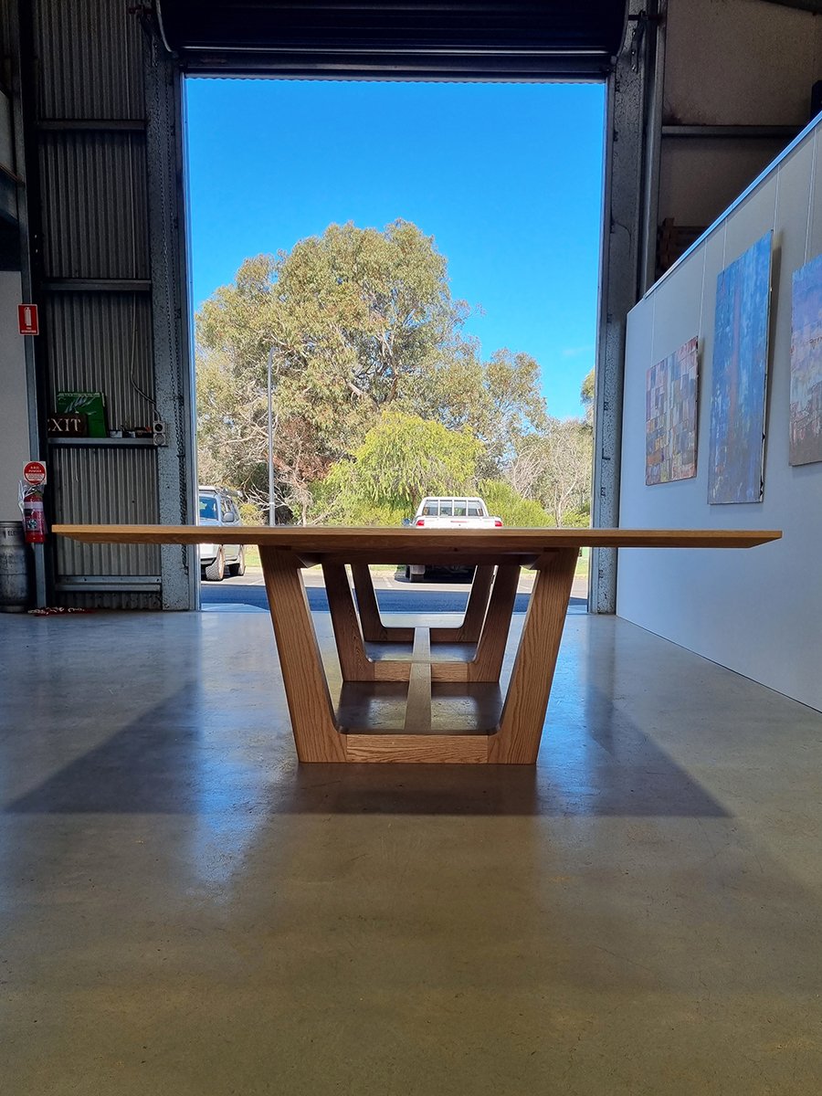 Rhodes House Boardroom Table in American Oak, trestle base design - Nathan Day Design, end view framed by open workshop doorway
