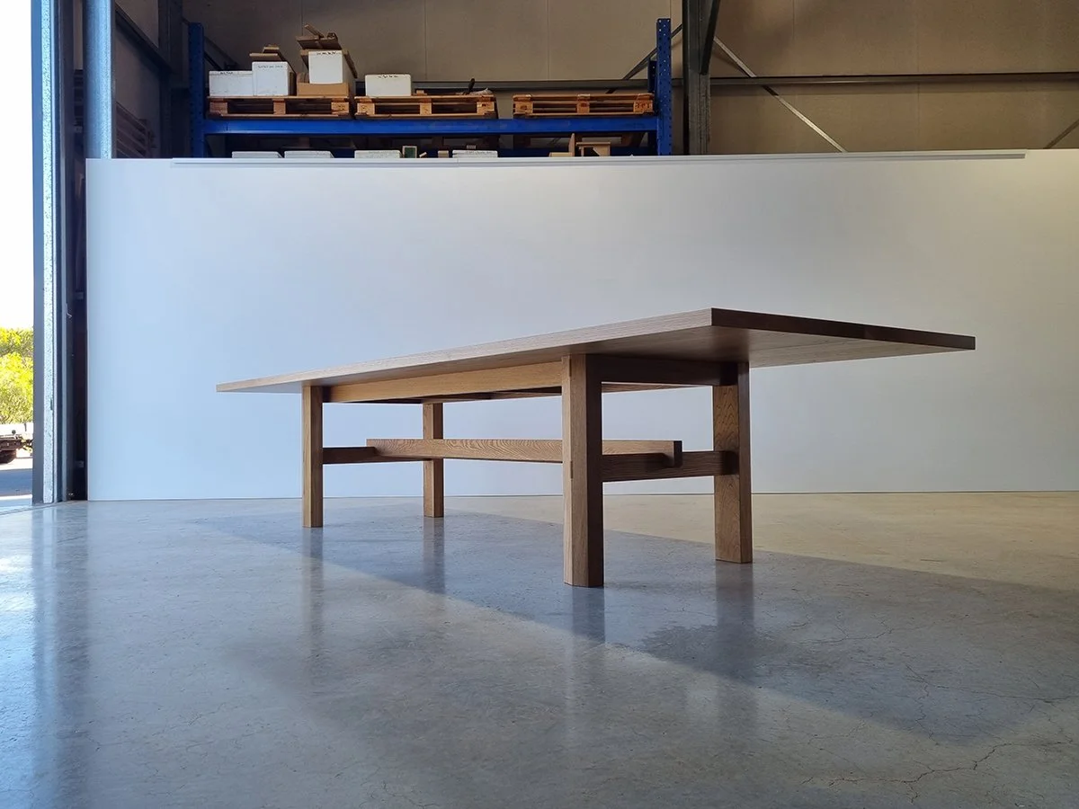 Angled view of Laura's Table showing classic farmhouse leg frame and stretcher rail in French Oak, near workshop doorway - bespoke furniture by Nathan Day Design