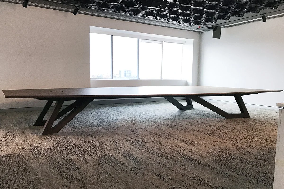 Satterley Boardroom Table in American Walnut, angular V-leg design - Nathan Day Design, front-on view in office space with geometric ceiling