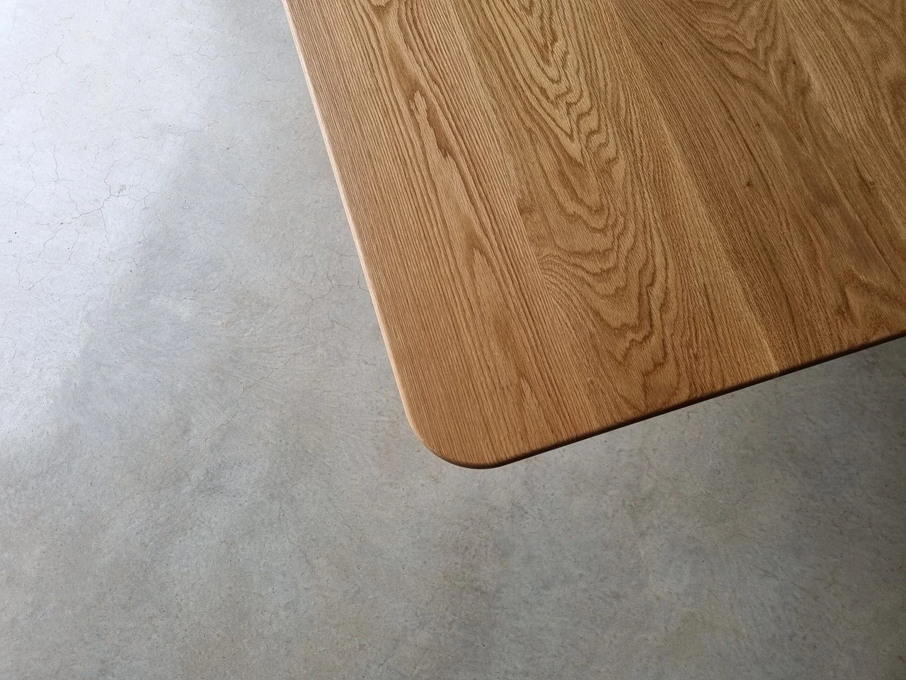 Close-up detail of Aalia Table's American Oak tabletop showing rounded corner and rich grain - bespoke furniture by Nathan Day Design