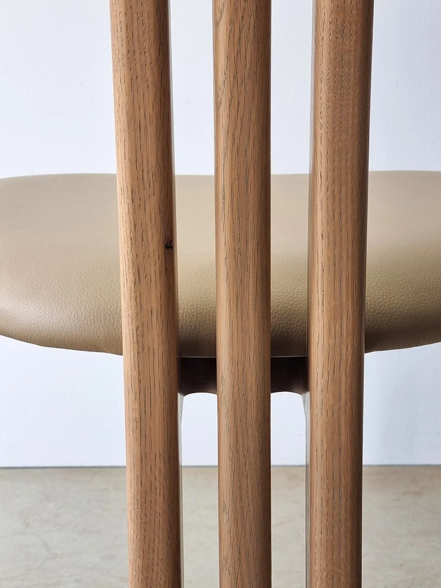 Close-up detail of Tulip Chair's three vertical Oak slat legs and tan leather seat pan, straight-on view - Nathan Day Design bespoke furniture