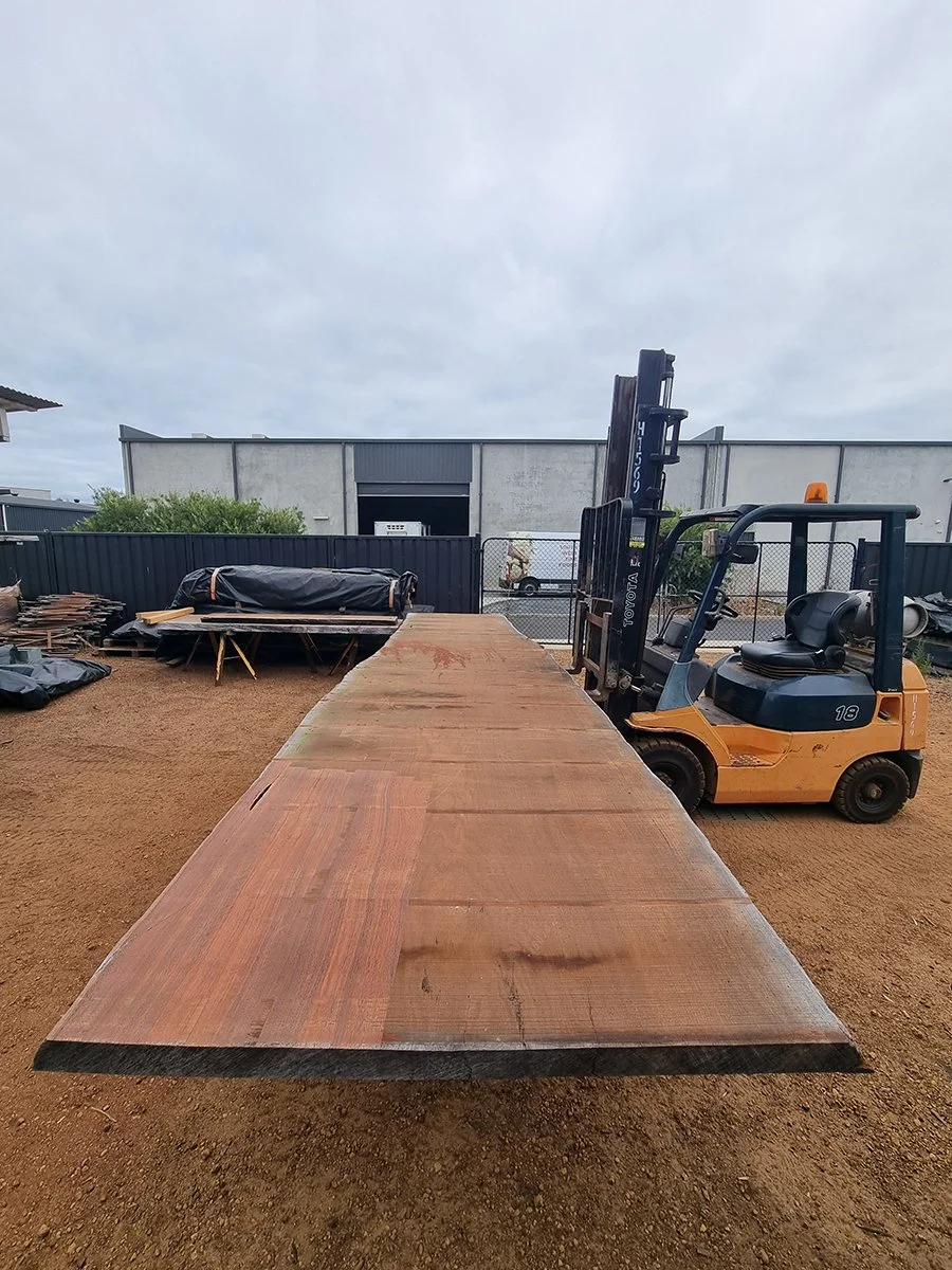 Massive raw timber slab laid out at the timber yard with forklift alongside, showing the scale of the live edge material - sourced for Nathan Day Design furniture
