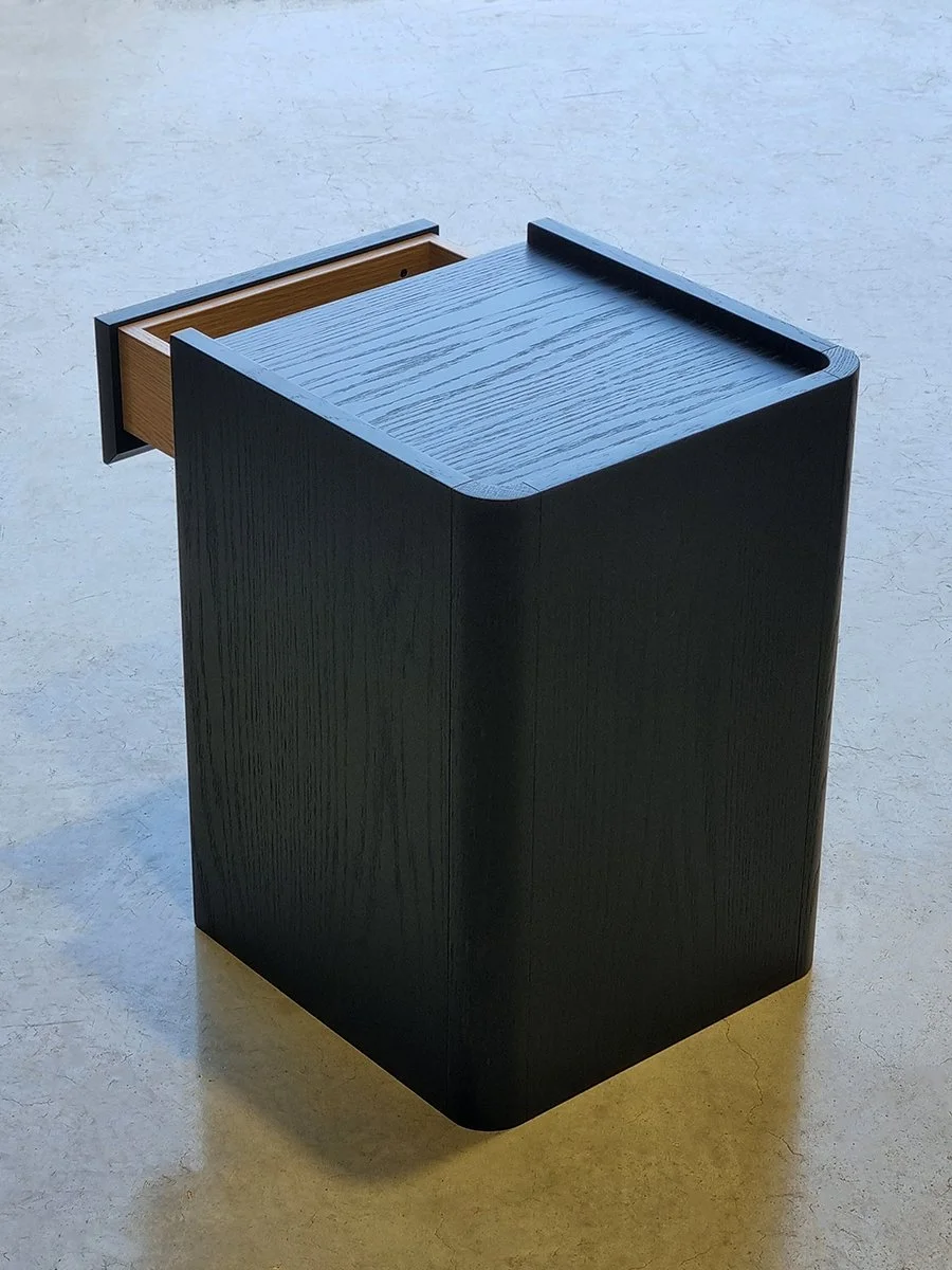 Majestic Close Bedside Table in ebonised Oak - Nathan Day Design, angled side view showing rounded top edge and open shelf