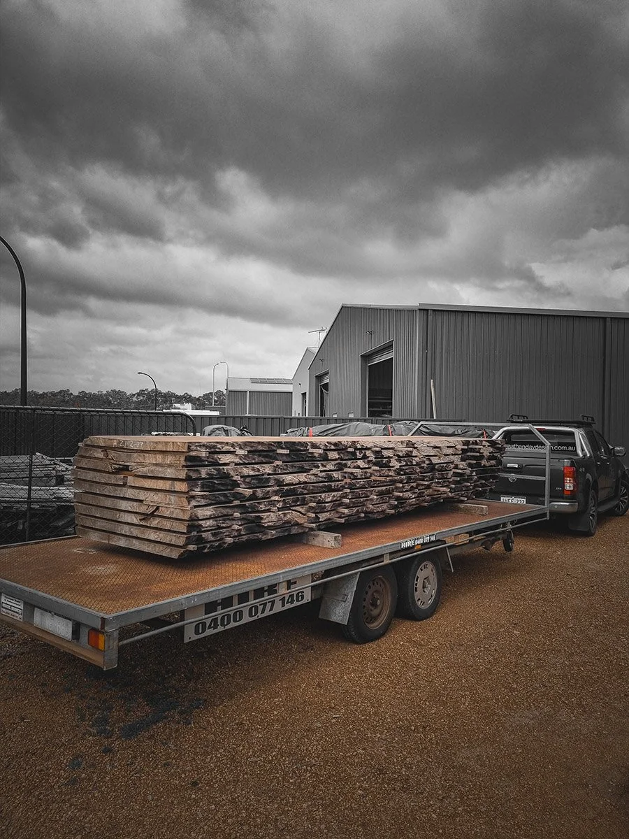Stack of raw live edge timber slabs loaded on delivery trailer under stormy sky, sourced for Nathan Day Design furniture