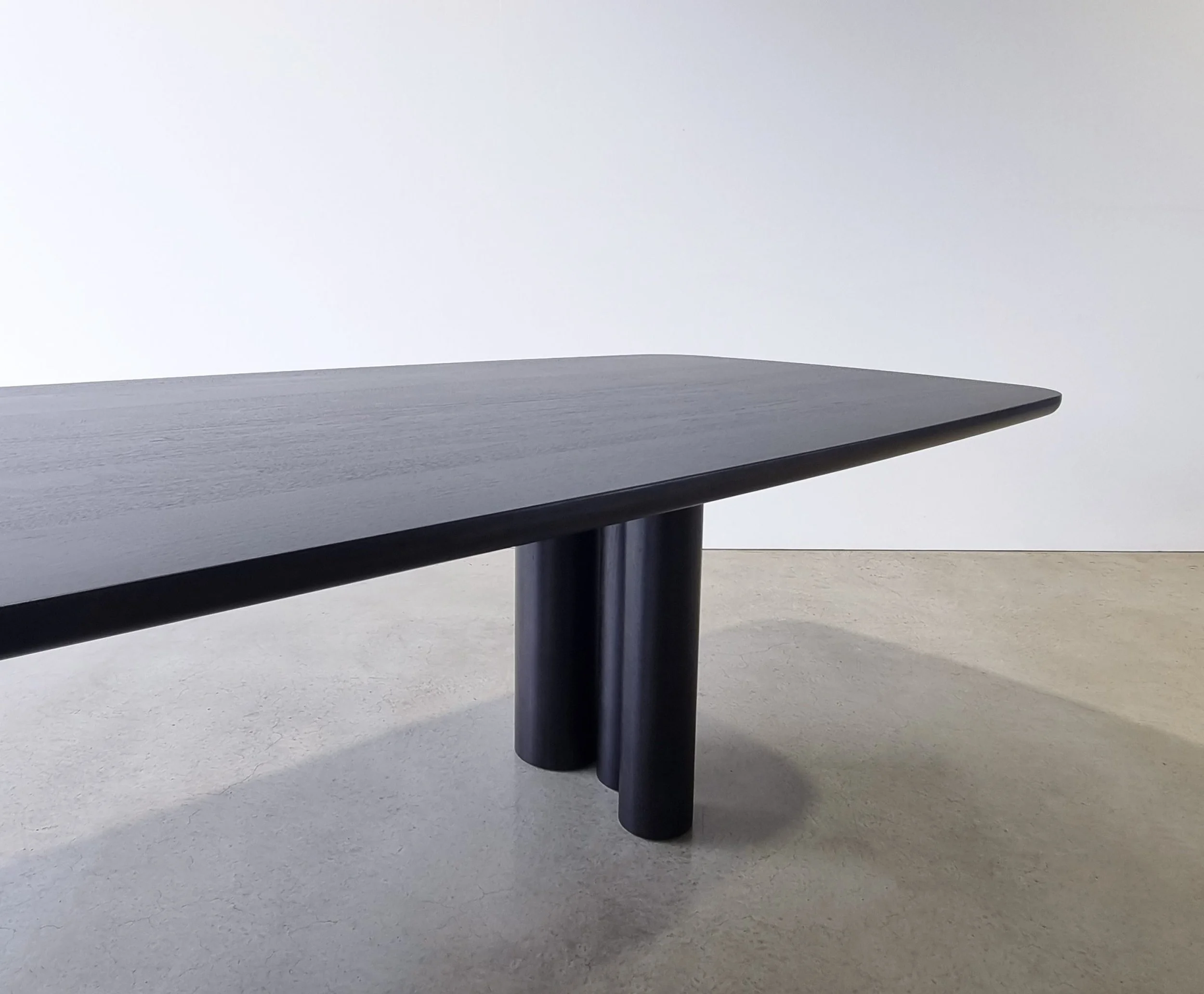Low-angle detail of Column Table's clustered cylindrical leg group in Ebonised Walnut - bespoke furniture by Nathan Day Design