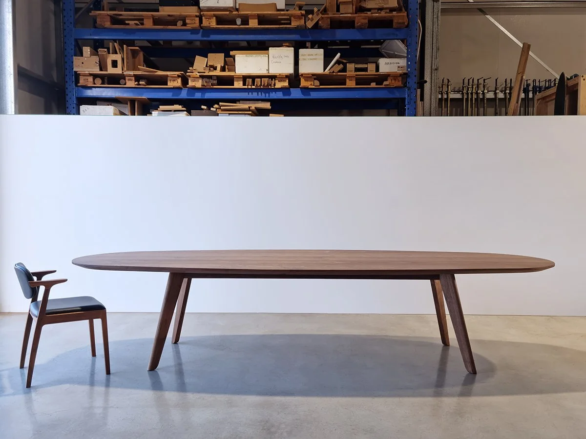 Peppy Grove Table oval dining table in Walnut with bevelled edge, paired with black leather dining chair in workshop setting - bespoke furniture by Nathan Day Design