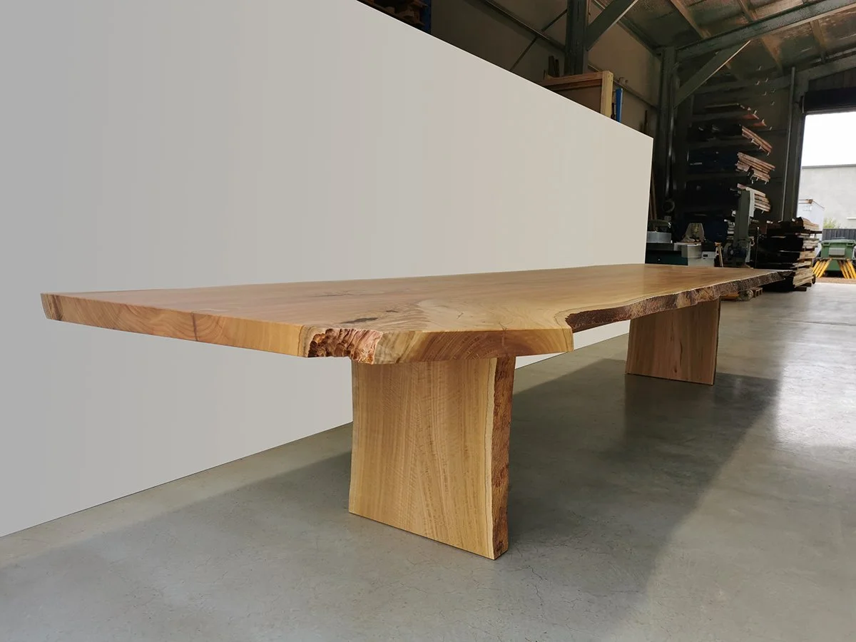 Wide live edge dining table in pale Tuart with slab-form legs, workshop setting with timber racking behind - bespoke furniture by Nathan Day Design