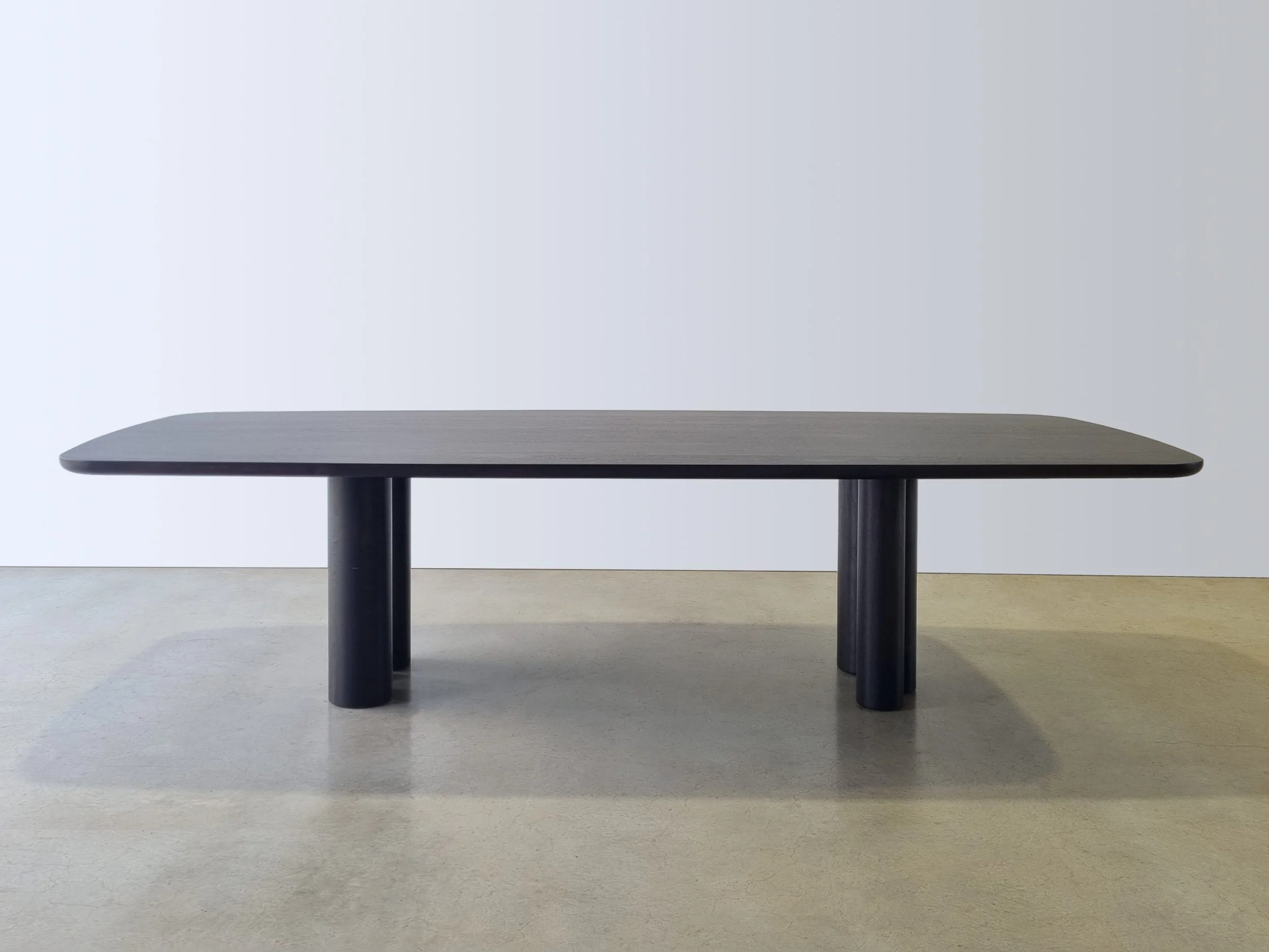 Column Table in Ebonised Walnut with sculptural asymmetrical column legs, front-on view in plain studio setting - bespoke dining table by Nathan Day Design