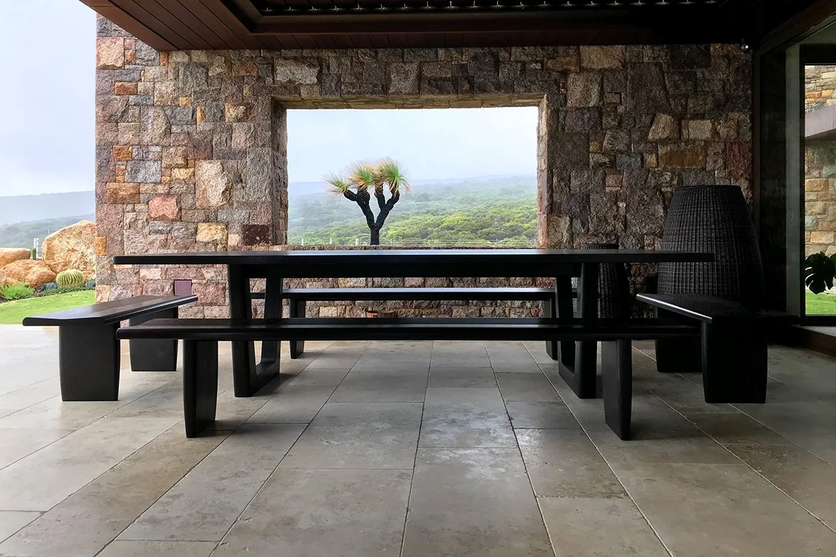Clairault Table in Ebonised Jarrah with matching bench seats, outdoor alfresco setting framed by a stone archway with landscape view - bespoke furniture by Nathan Day Design