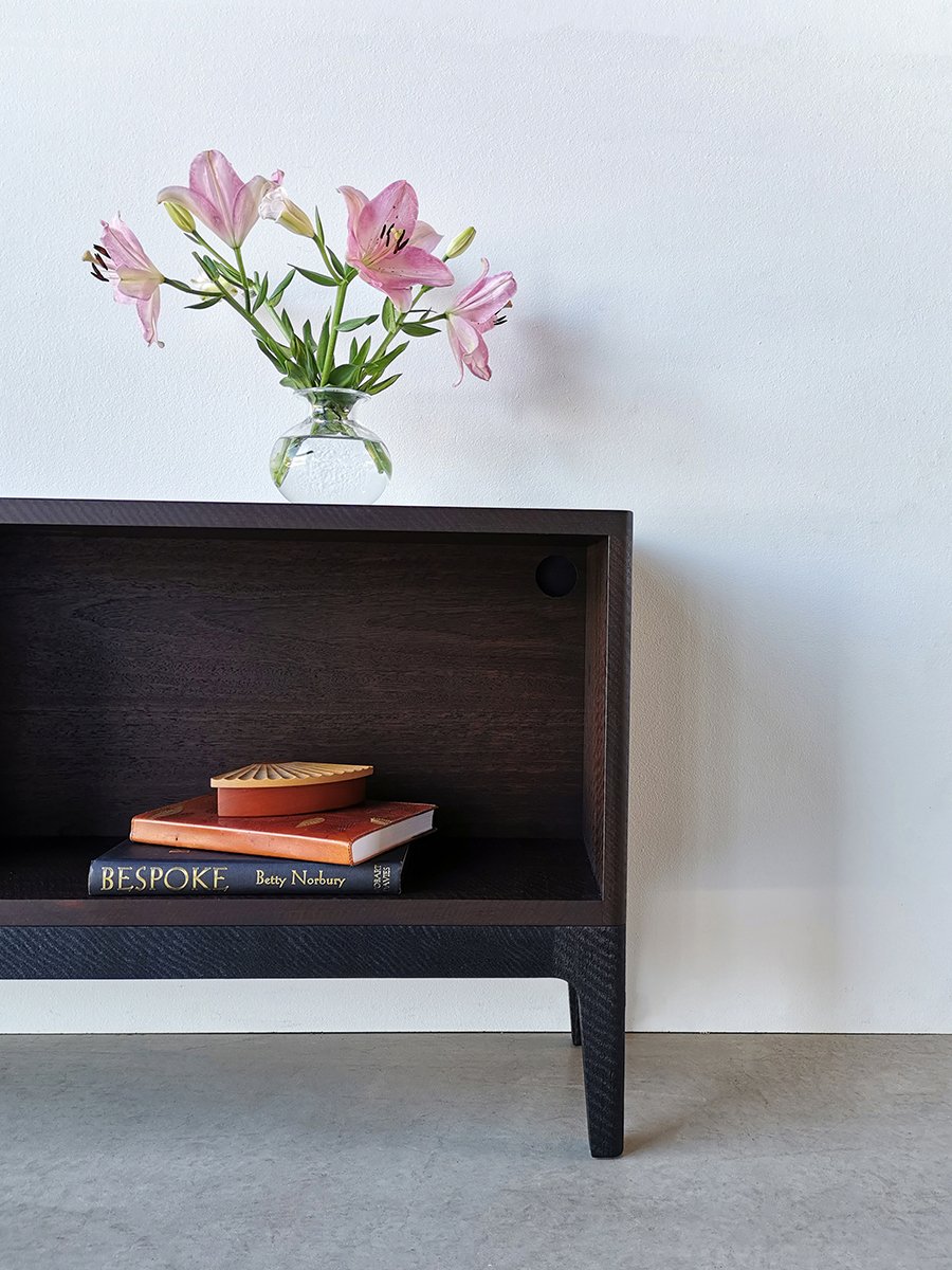 Sally's Bookcase in ebonised and scorched Jarrah, angled front view styled with lily flowers and books - Nathan Day Design