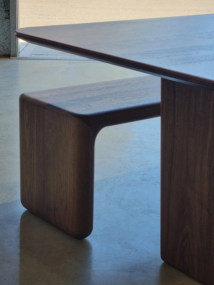 Hippo Bench in Walnut tucked beneath a matching dining table, near workshop doorway - bespoke seating by Nathan Day Design
