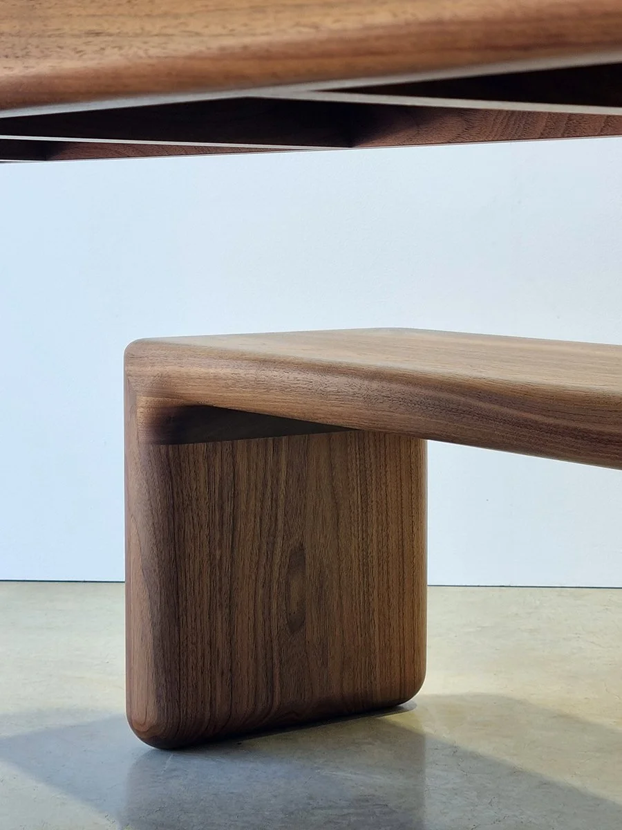 Angled view of Hippo Bench in Walnut showing the waterfall-edge leg meeting the seat surface, positioned beneath a dining table - bespoke seating by Nathan Day Design