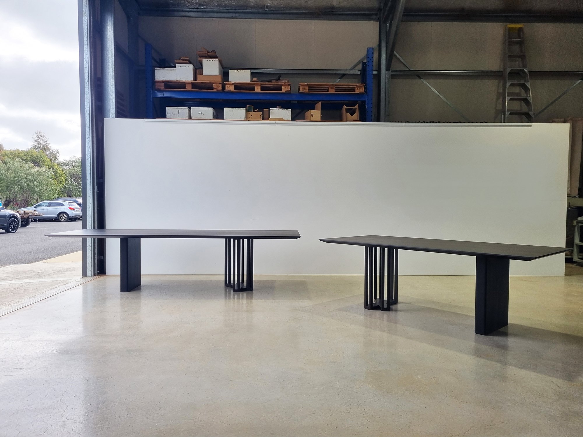 Two Giacci Table variants shown side by side in the workshop with mirrored asymmetrical legs - Nathan Day Design