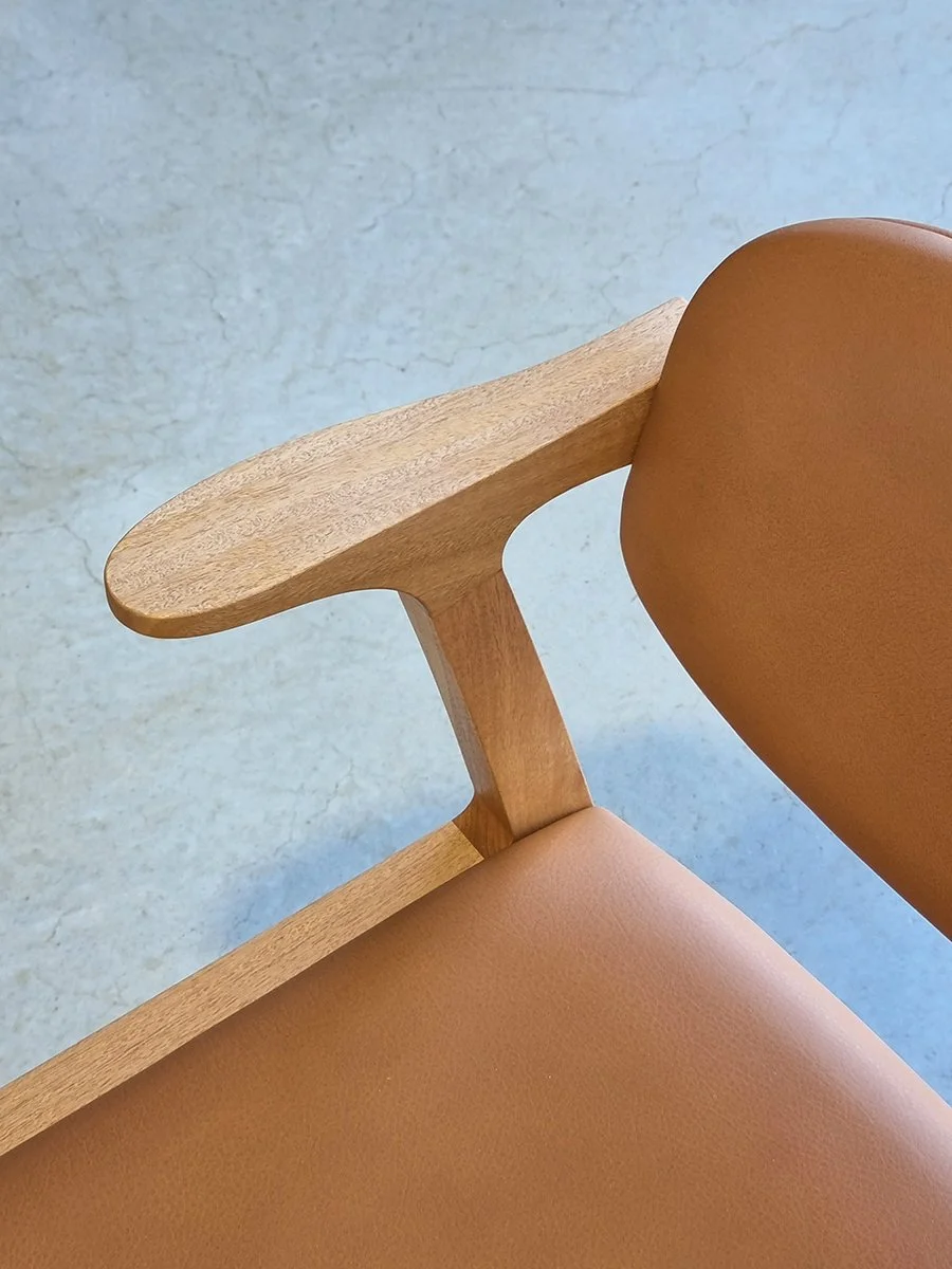 Close-up detail of Kinross Chair's sculptural armrest joinery in timber and tan leather upholstery - bespoke furniture by Nathan Day Design