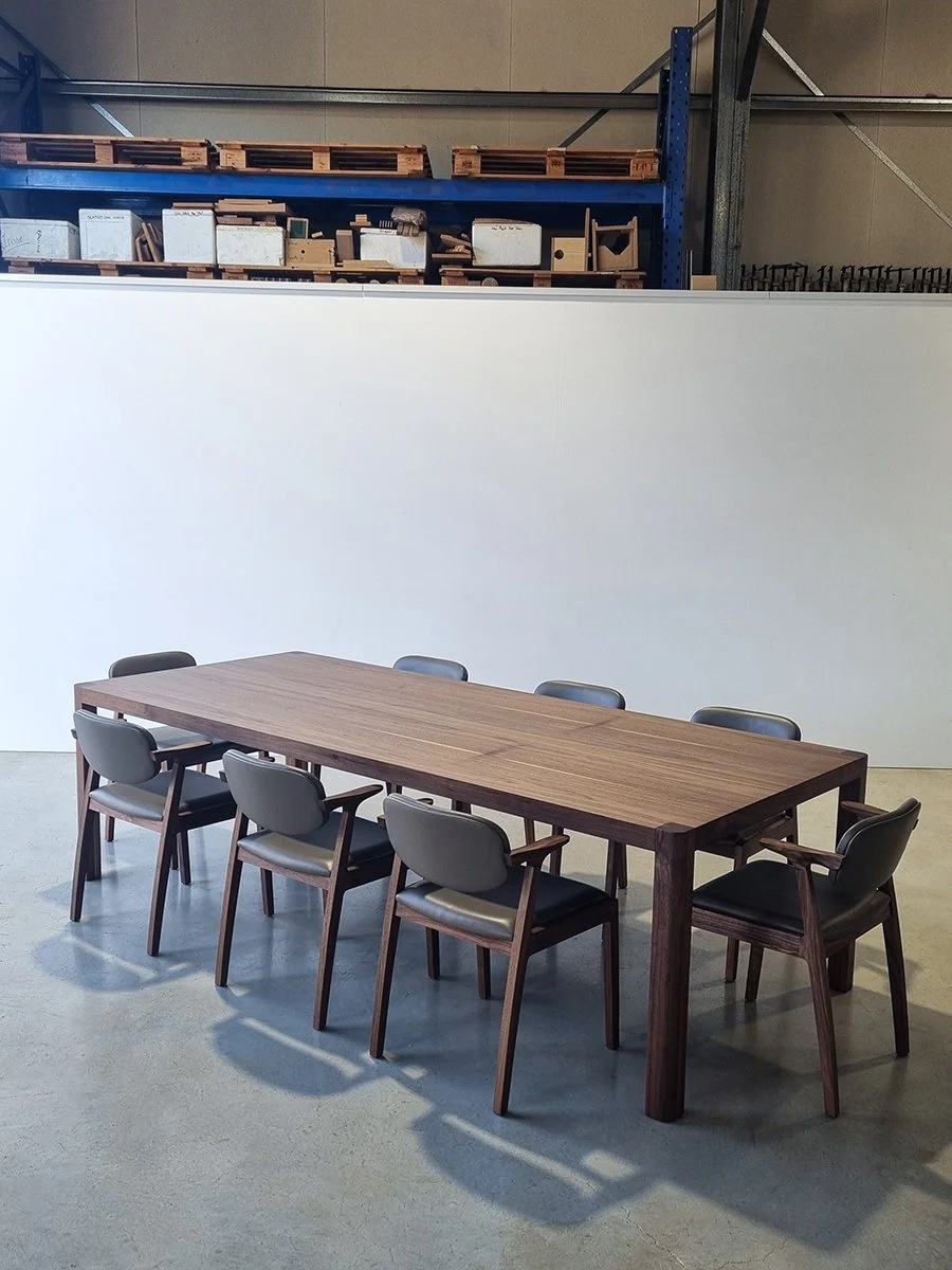 Irvine Table in American Walnut set with eight grey upholstered dining chairs in workshop setting - bespoke furniture by Nathan Day Design