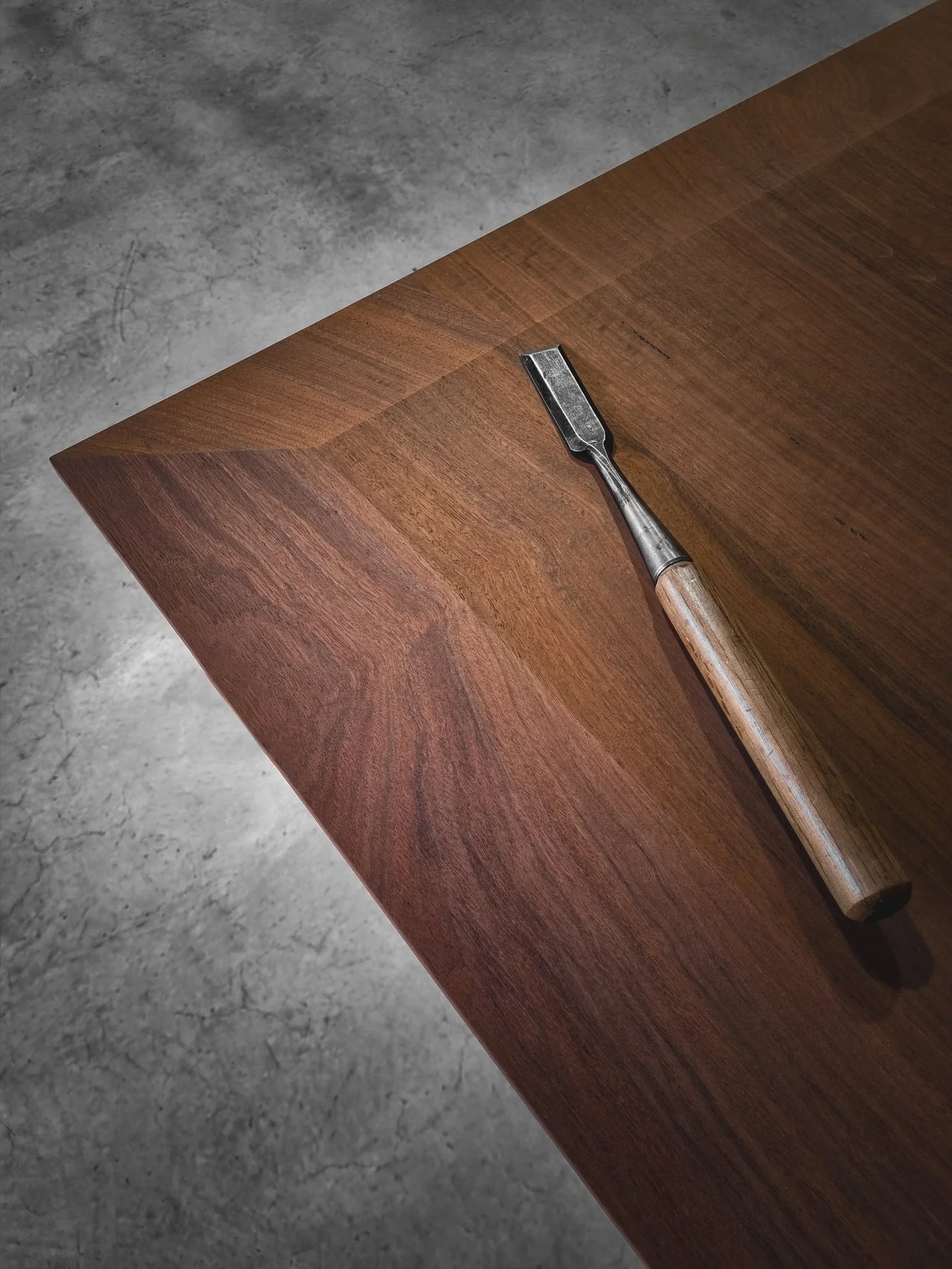 A woodworking chisel resting on richly grained hardwood, a detail of hand-tool craftsmanship at Nathan Day Design