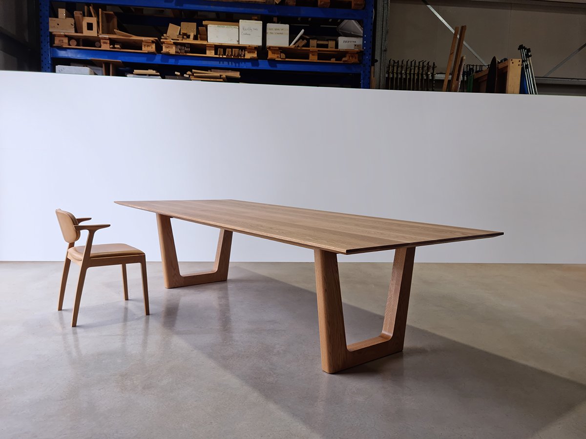 Full angled view of Clairault Table in American Oak paired with a matching timber-armed dining chair, workshop setting - bespoke furniture by Nathan Day Design