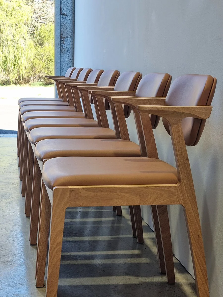 A long row of Kinross Chairs in tan leather and timber lined up in the workshop doorway with bushland view - bespoke furniture by Nathan Day Design