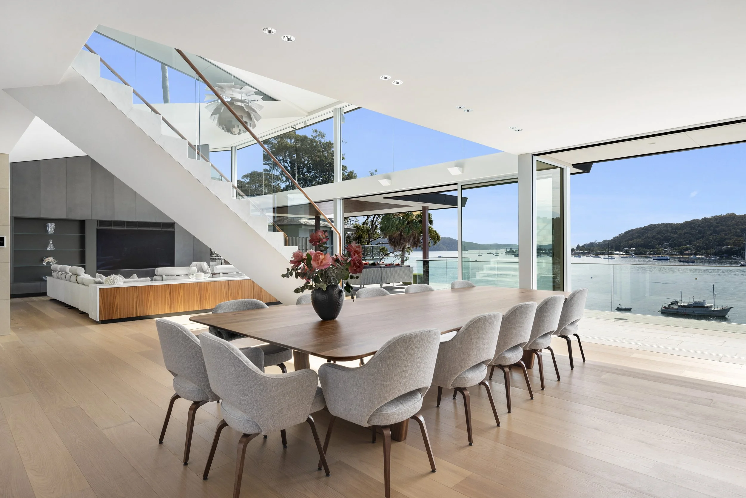 Cabarita Rd Table in Walnut set with grey upholstered chairs in a waterfront home, floor-to-ceiling glass overlooking Pittwater - bespoke furniture by Nathan Day Design