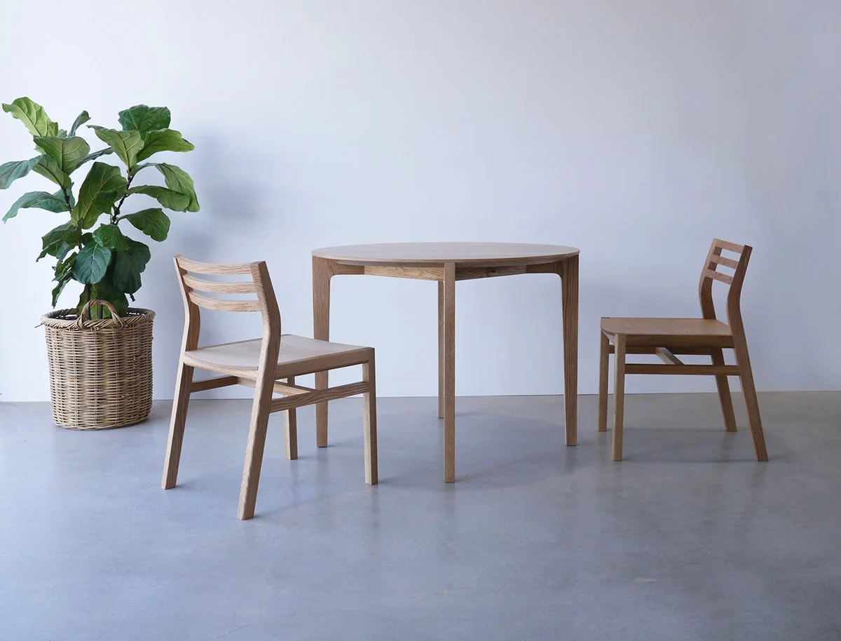 Pair of Walter Dining Chairs in American Oak flanking a small square dining table, plain studio setting with potted plant - bespoke furniture by Nathan Day Design