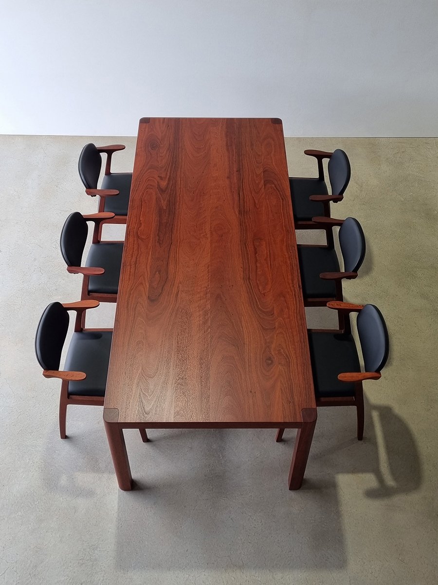Overhead view of Irvine Table in American Walnut set with six black leather dining chairs, showcasing rich timber grain - bespoke furniture by Nathan Day Design